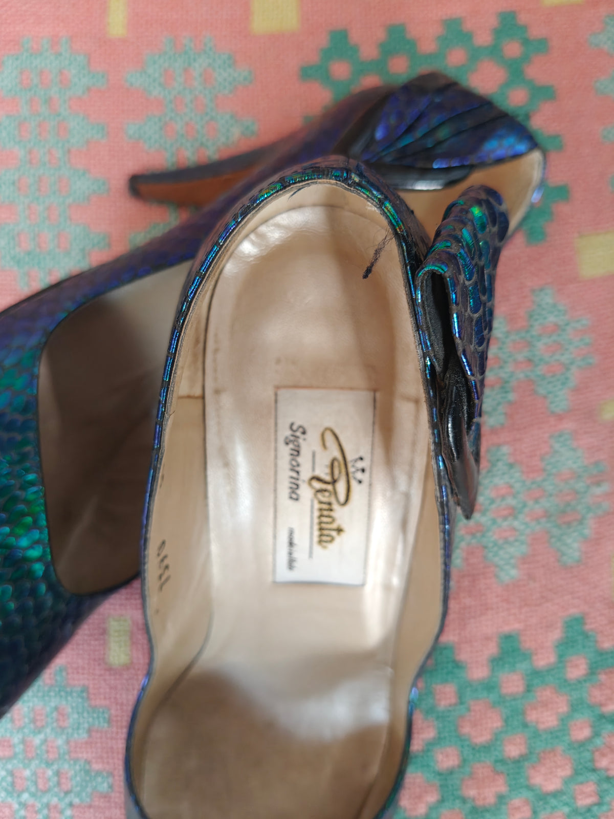 A close-up of a 80's blue and green iridescent snakeskin-patterned high-heeled shoe, showing the insole with the 'Renata' brand label, resting on a pink and teal patterned fabric background.
