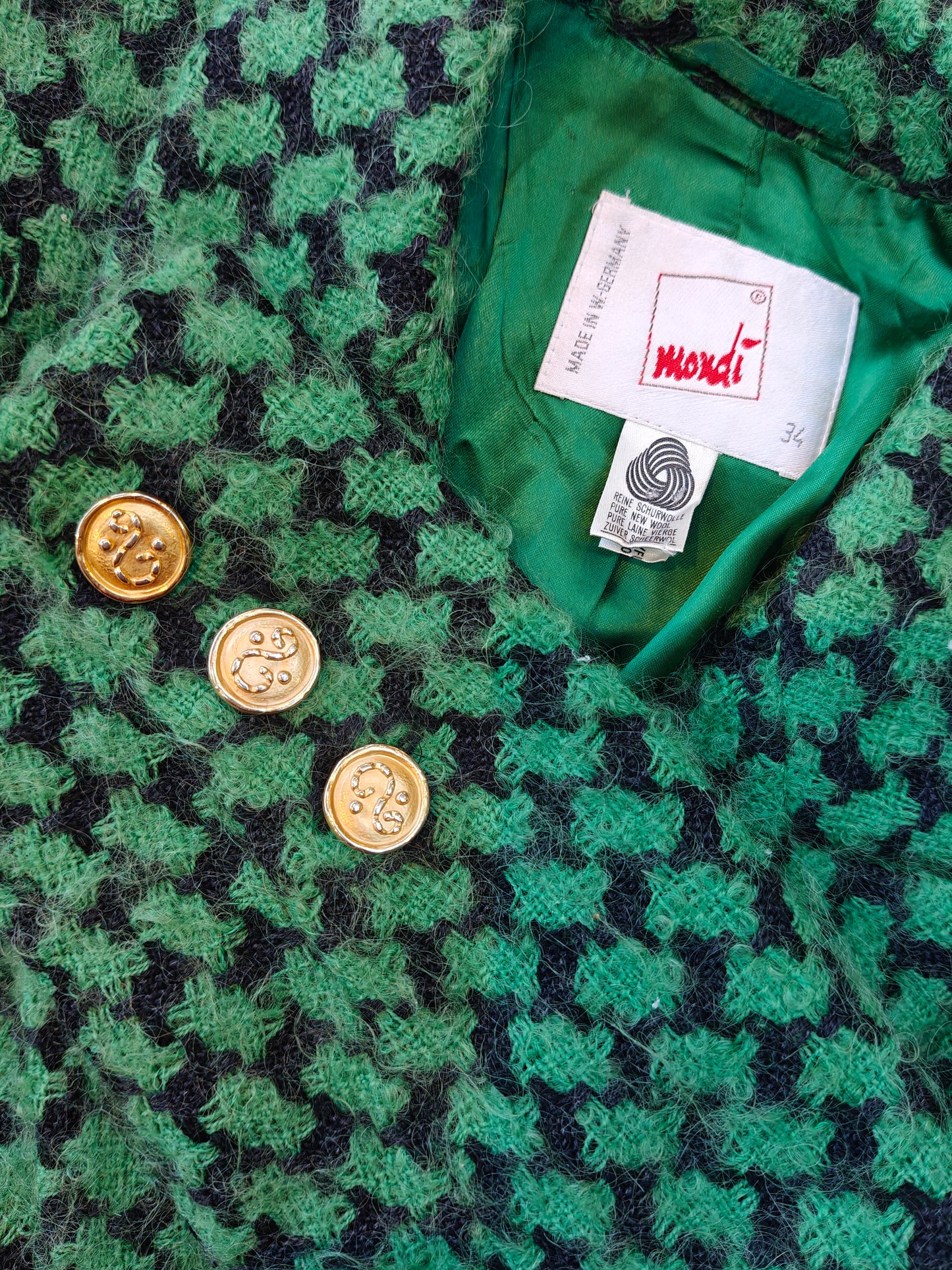 Green textured fabric with gold buttons and a Mondi label.