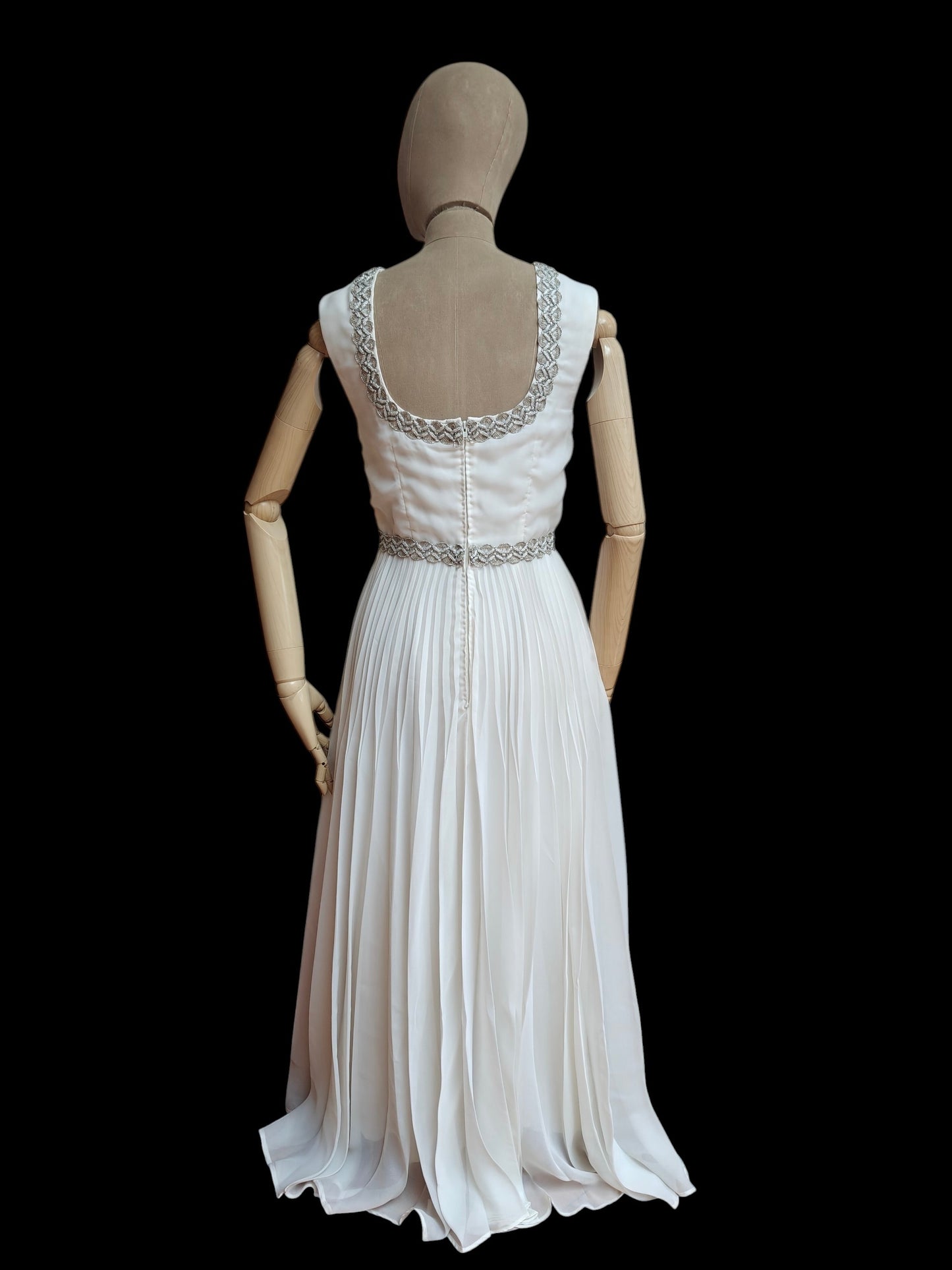 White vintage evening gown with beaded detailing on a mannequin against a black background