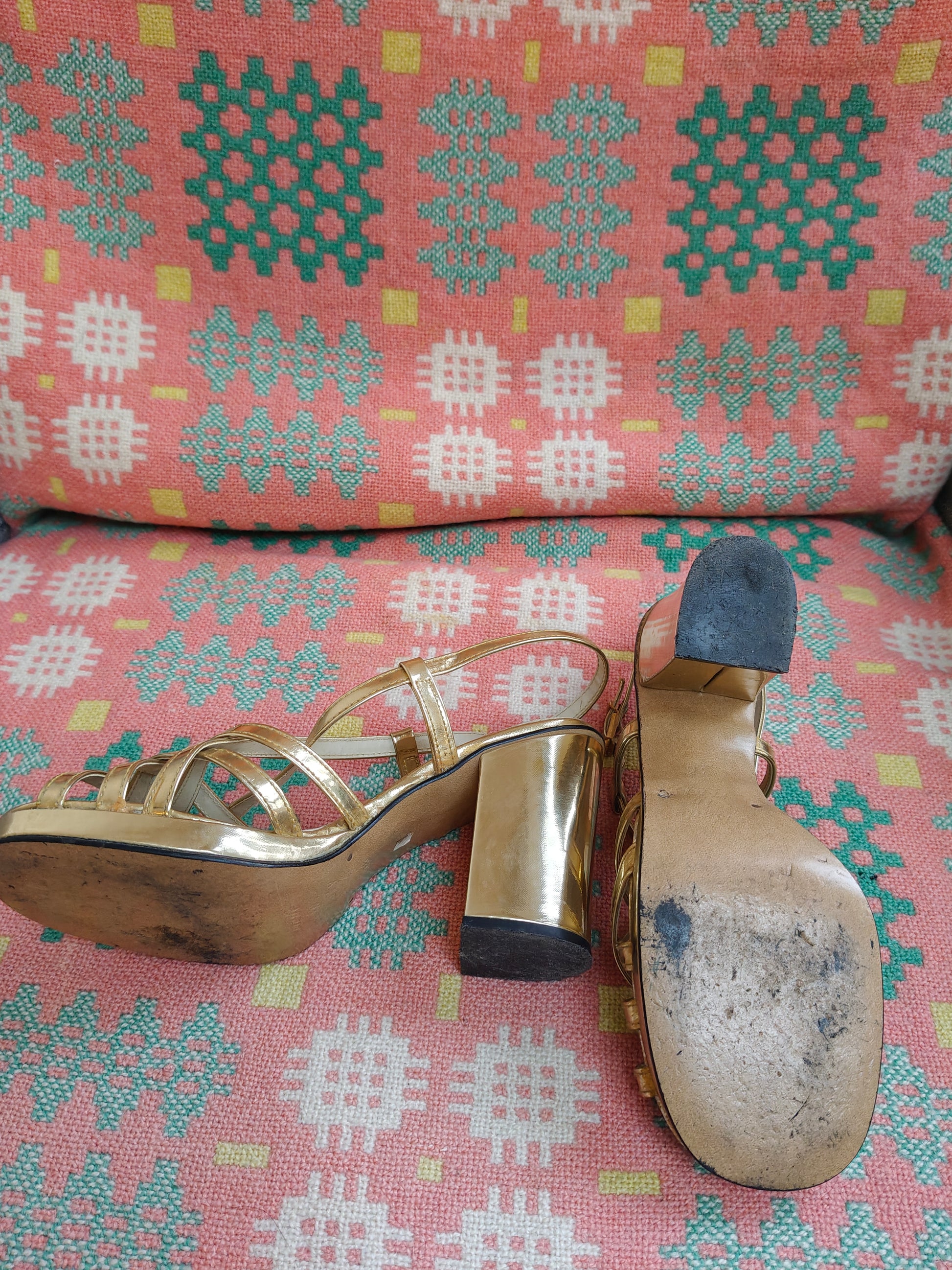 Gold high-heeled shoe with a worn sole on a pink patterned surface