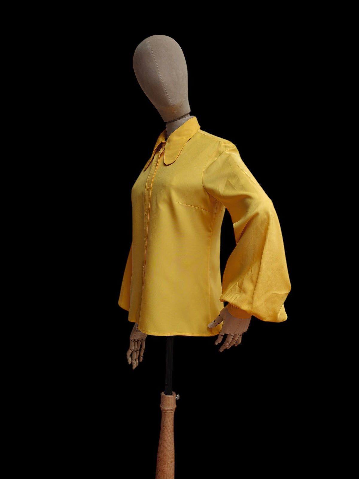 A bright yellow long-sleeve vintage blouse displayed on a mannequin against a solid black background.