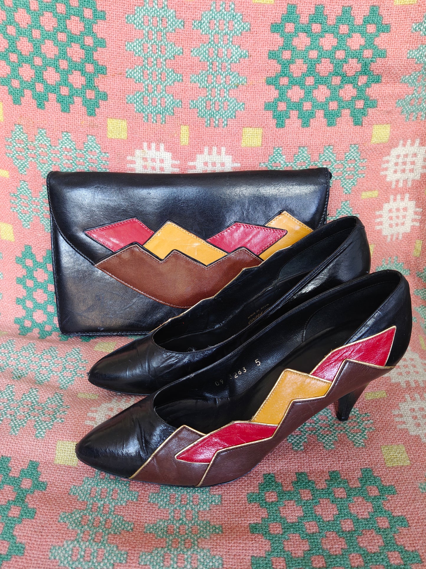 Black 80's shoes with colourful pattern and a matching clutch on a patterned fabric background