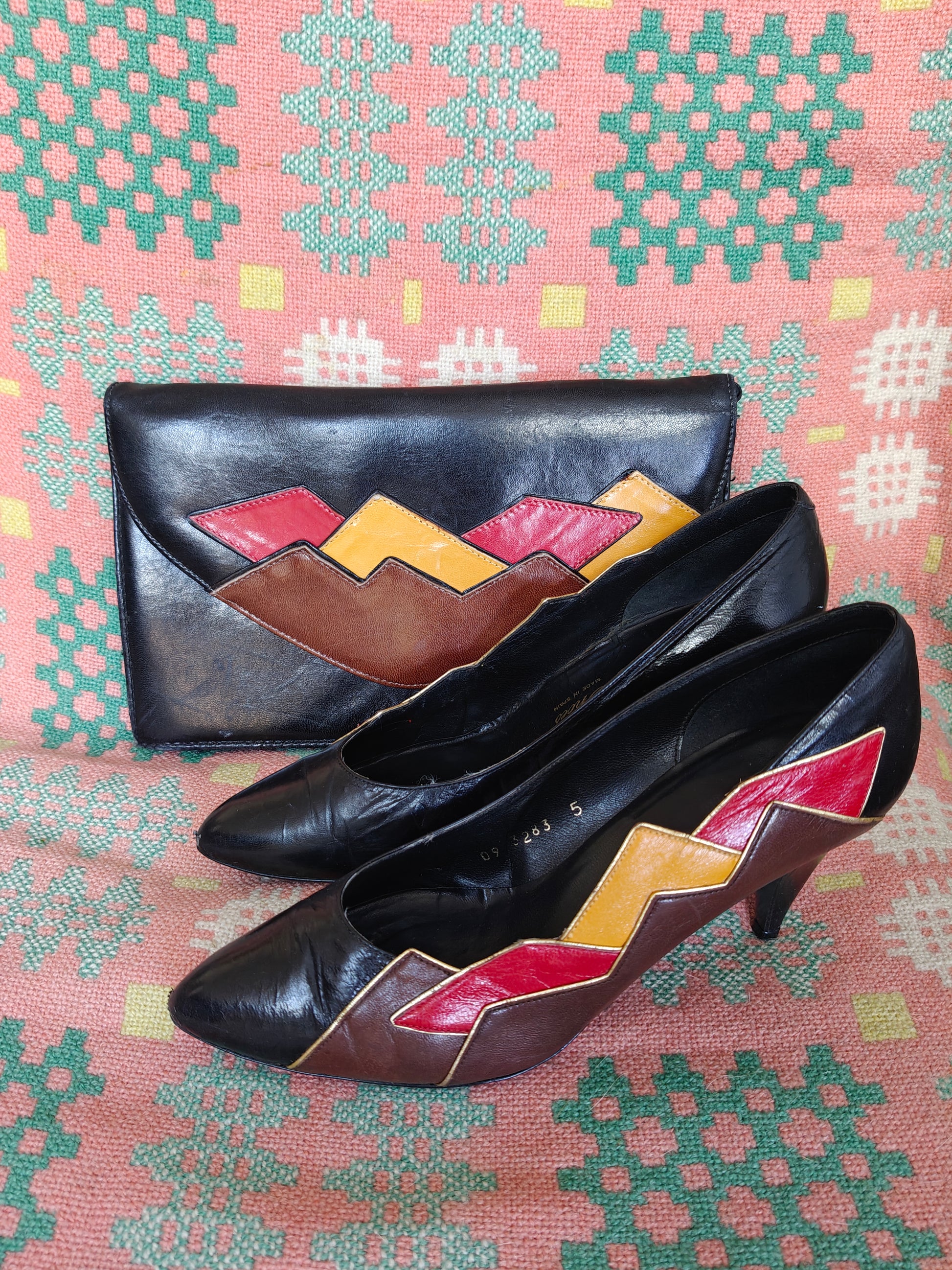 Black 80's shoes with colourful pattern and a matching clutch on a patterned fabric background
