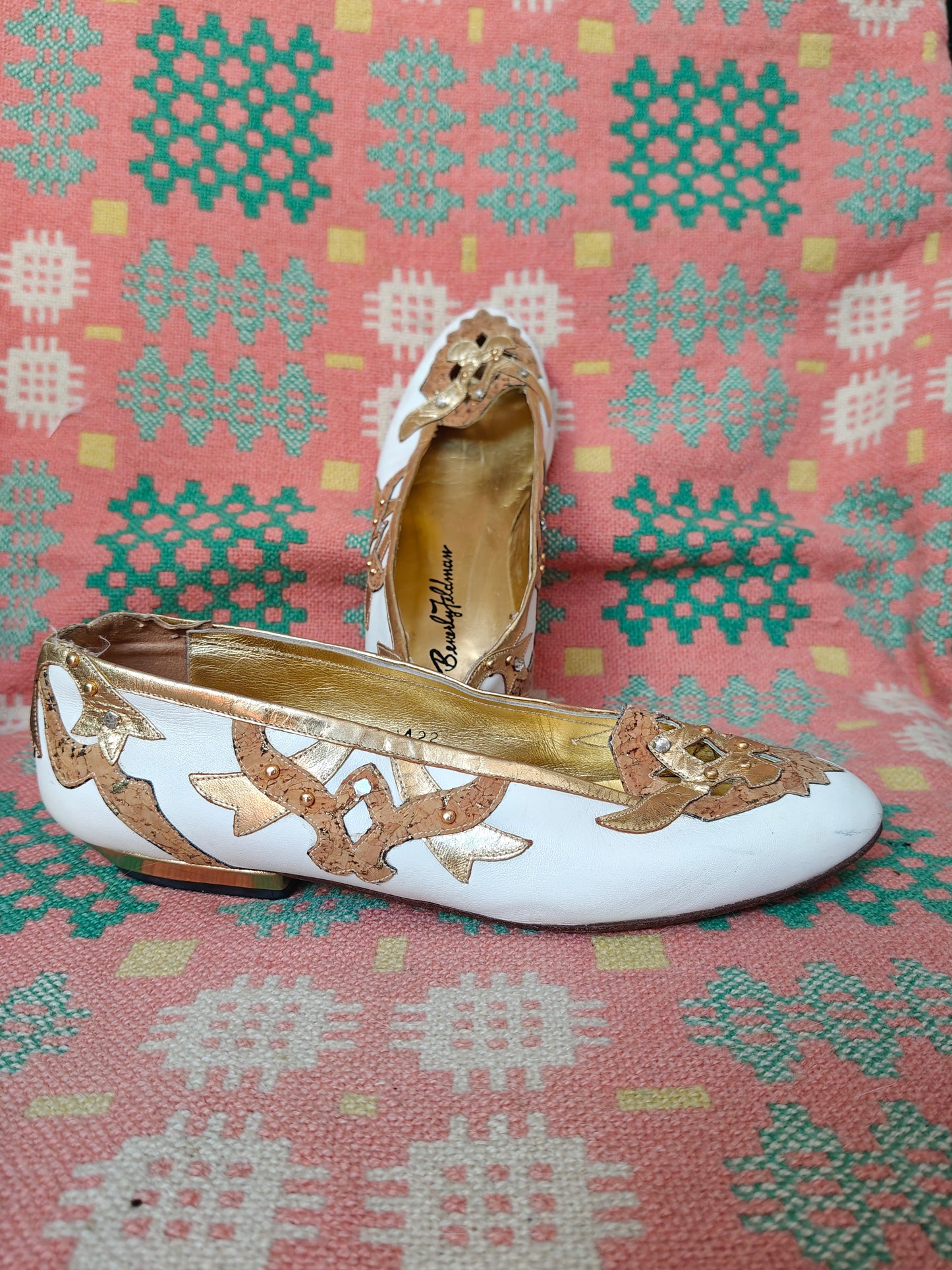 White and gold flat shoes on a patterned fabric background