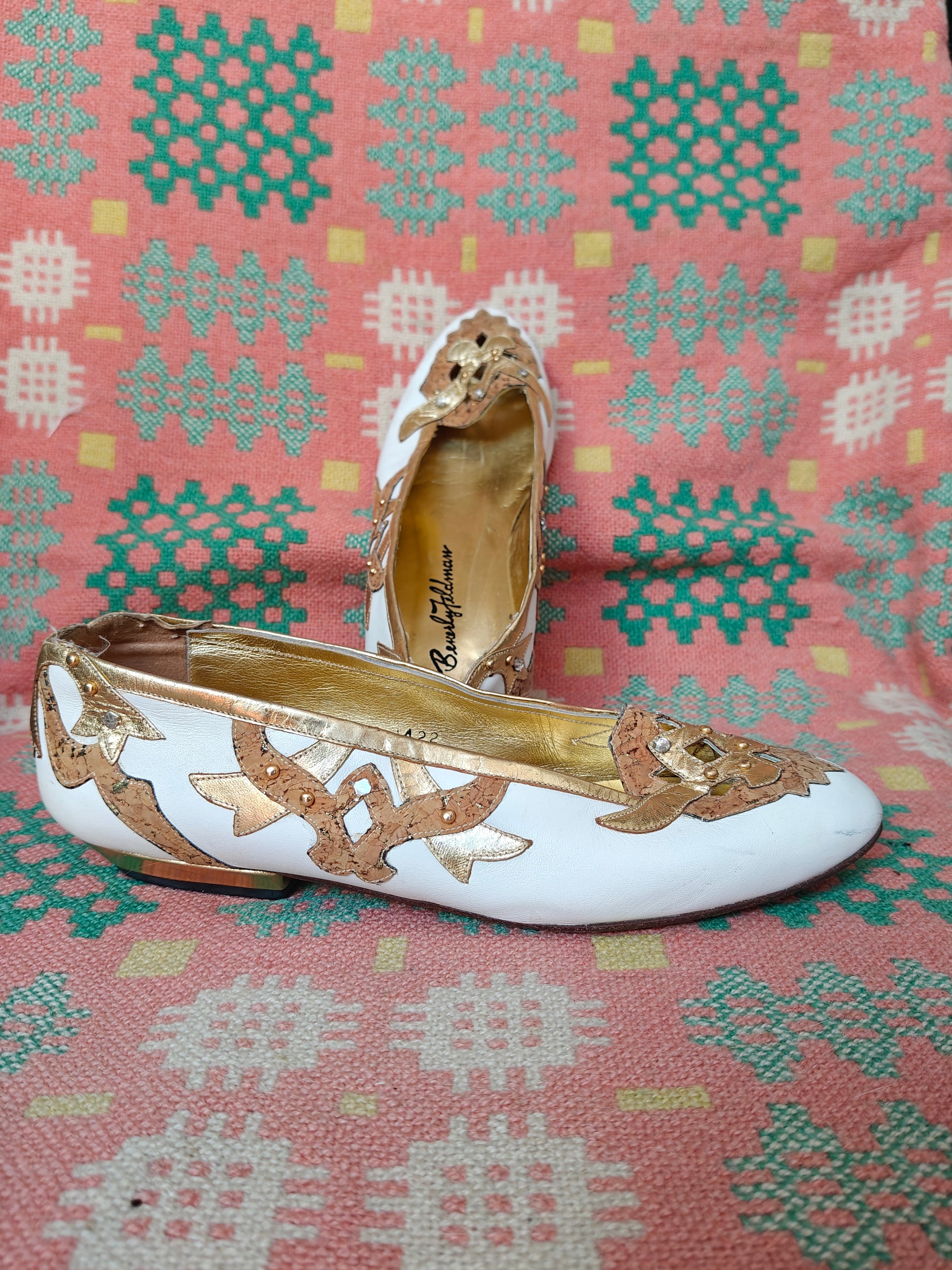 White and gold flat shoes on a patterned fabric background