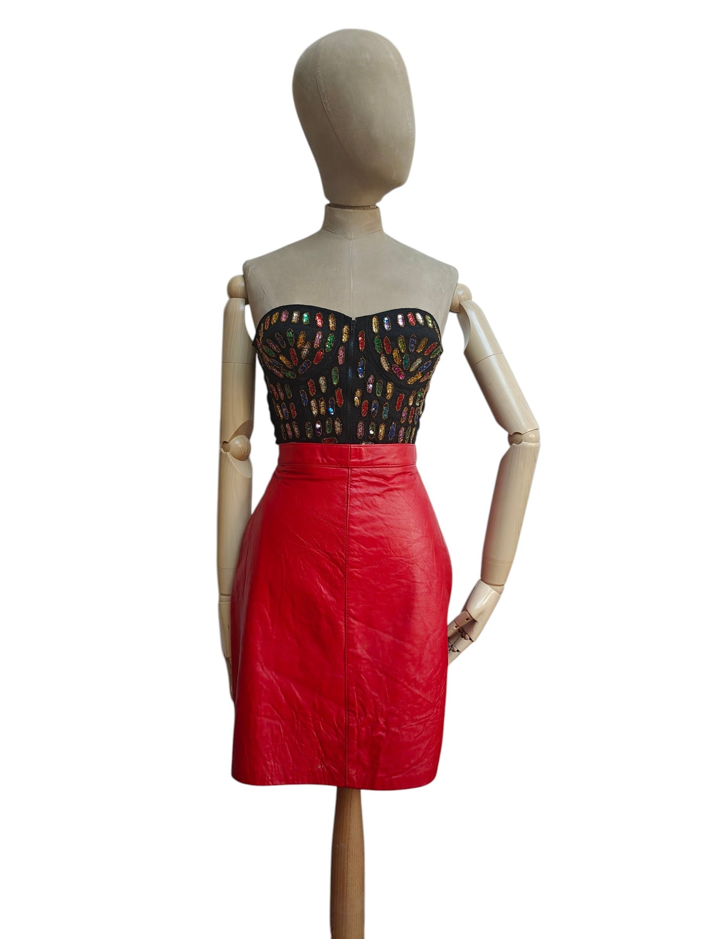 A two-piece women's outfit displayed on a wooden mannequin against a white background. The set includes a strapless black top with a colorful geometric pattern and a high-waisted red faux-leather skirt.
