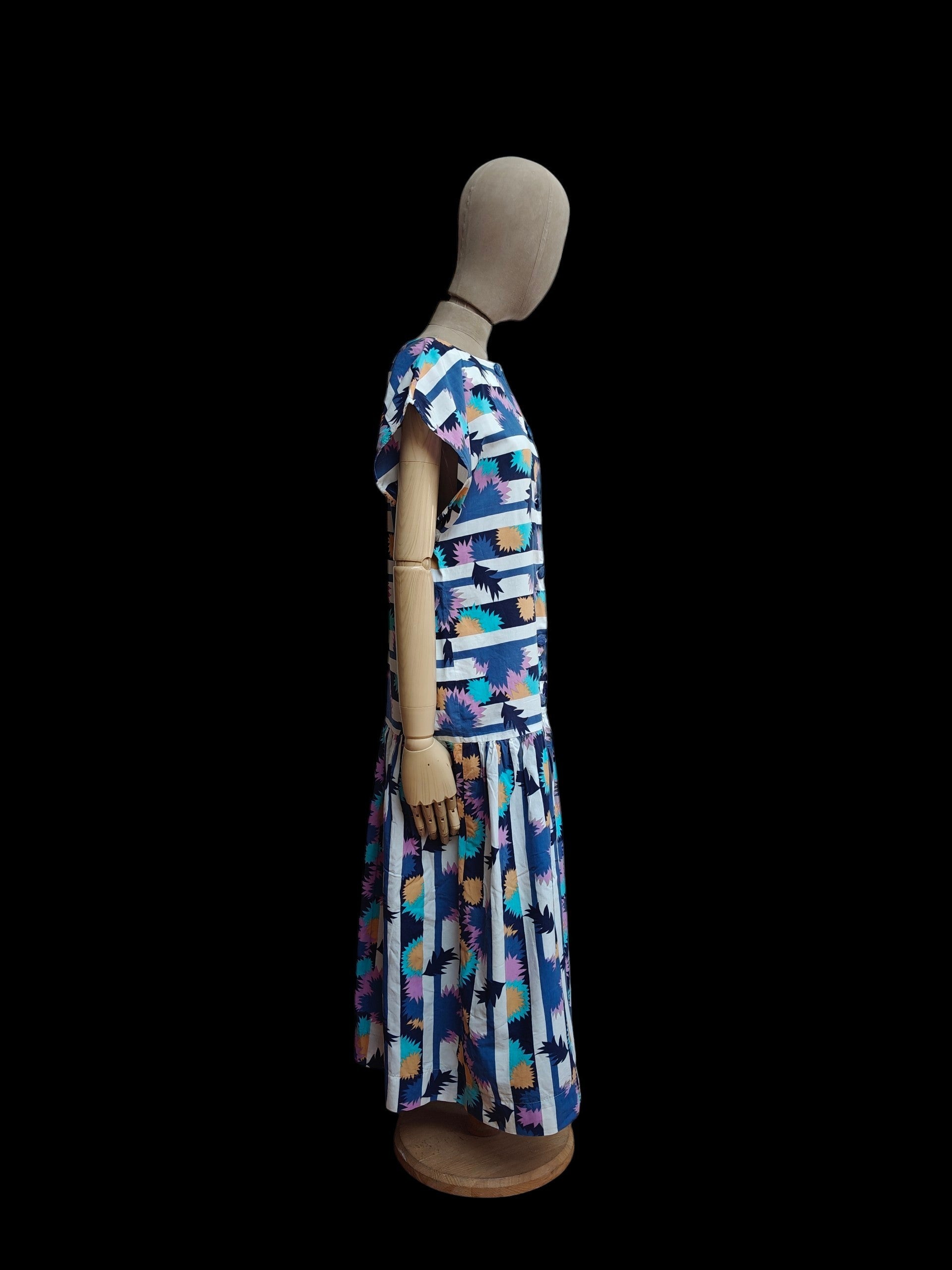 A short-sleeve maxi dress with a colourful abstract geometric print, displayed on a mannequin against a solid black background.
