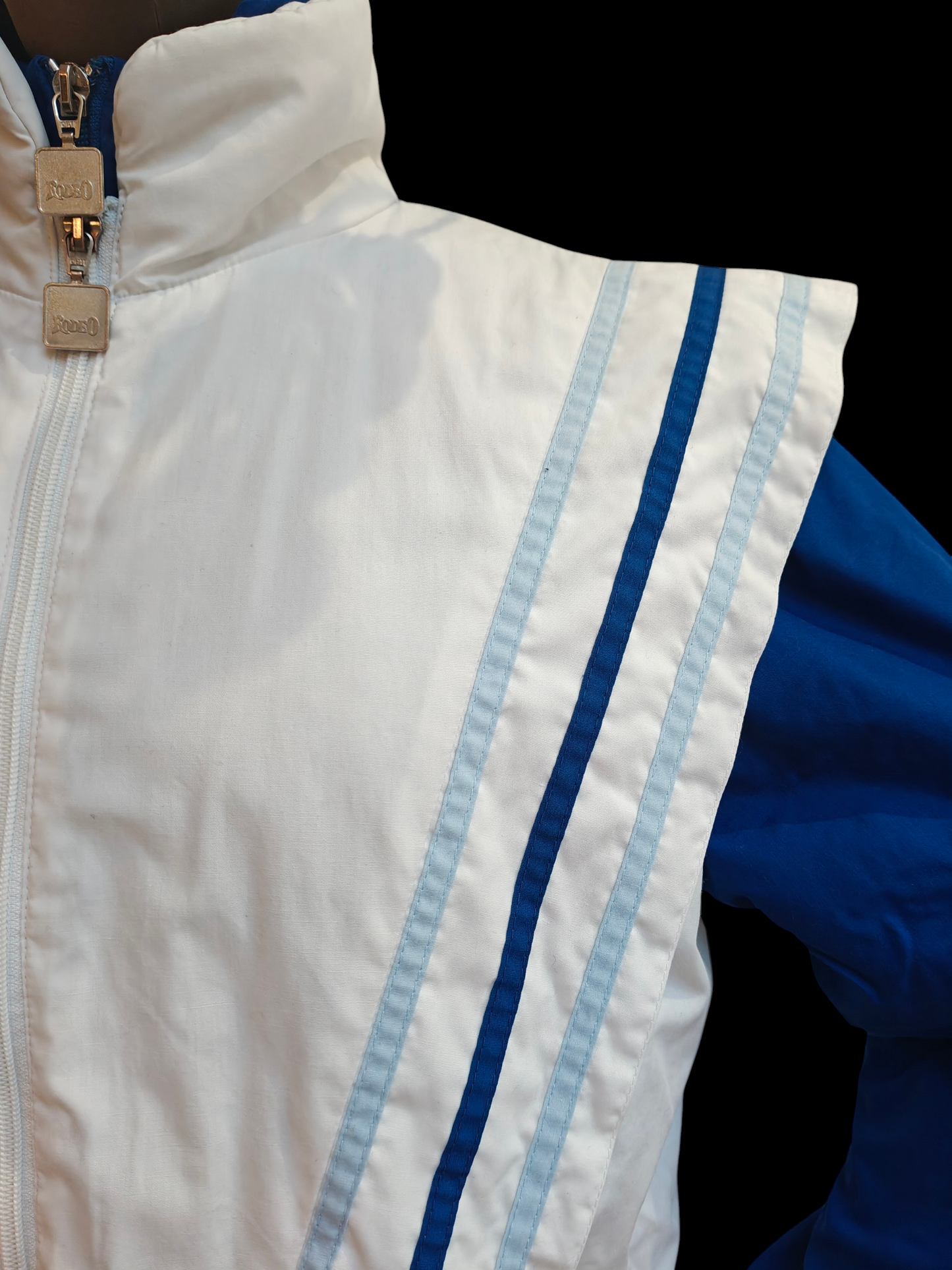 Close-up of a white jacket with blue accents and a gold zipper on a black background