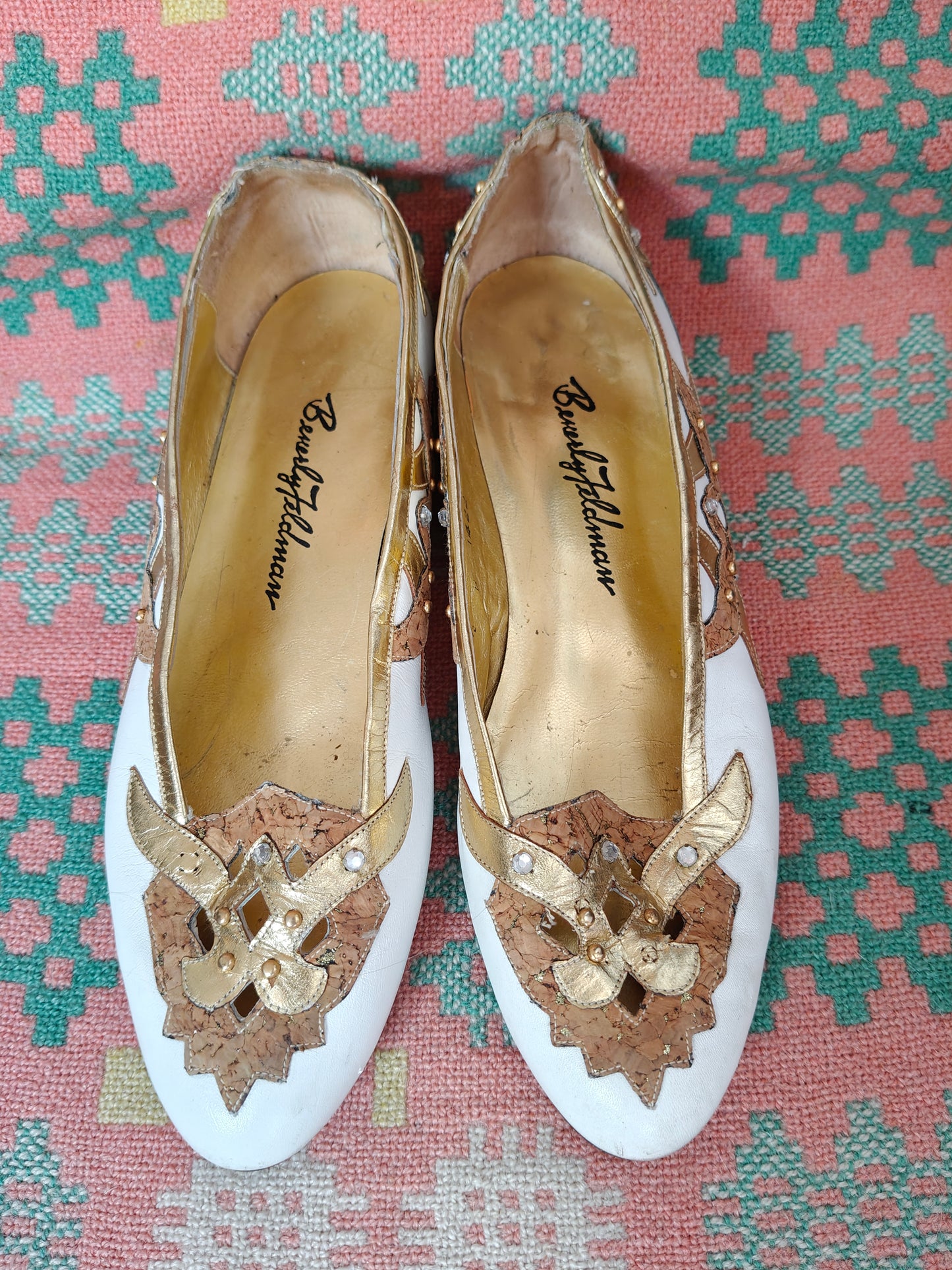 Pair of decorative shoes with gold embellishments on a patterned fabric background