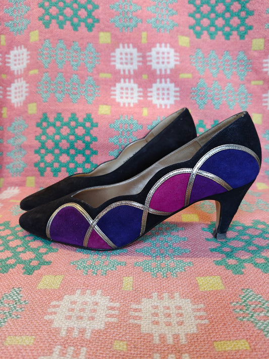 Black high-heeled shoes with purple and blue geometric design on a patterned pink background