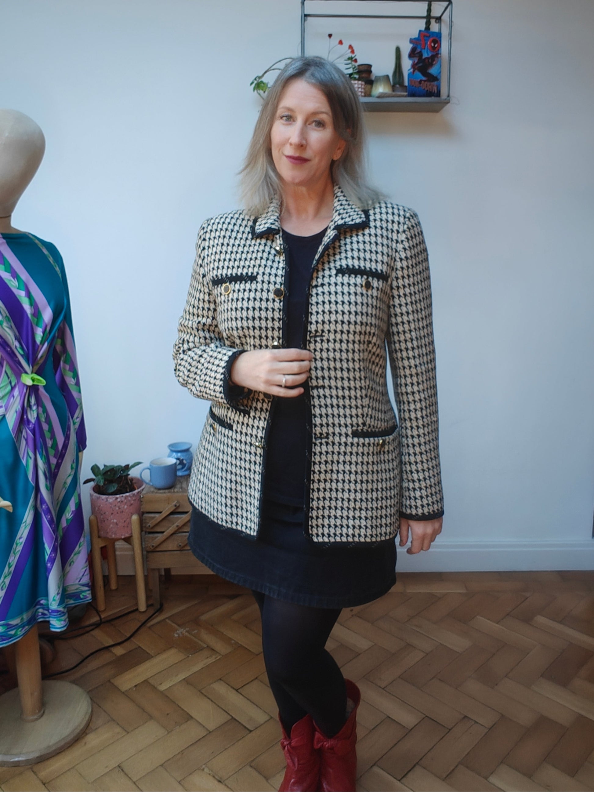 Woman wearing a houndstooth patterned jacket in a room with a mannequin and clothing items.