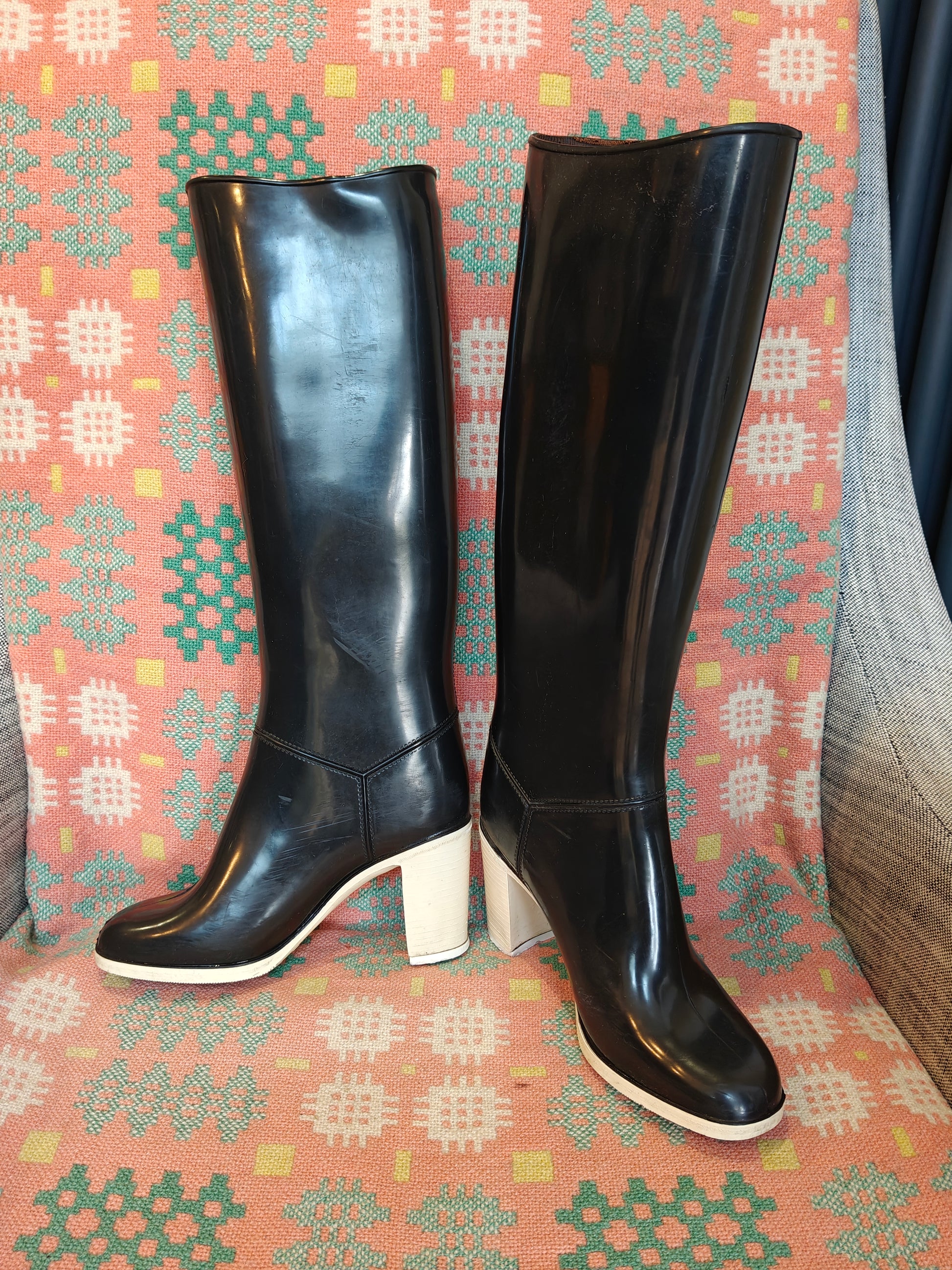 Black knee-high boots with white soles on a patterned fabric background