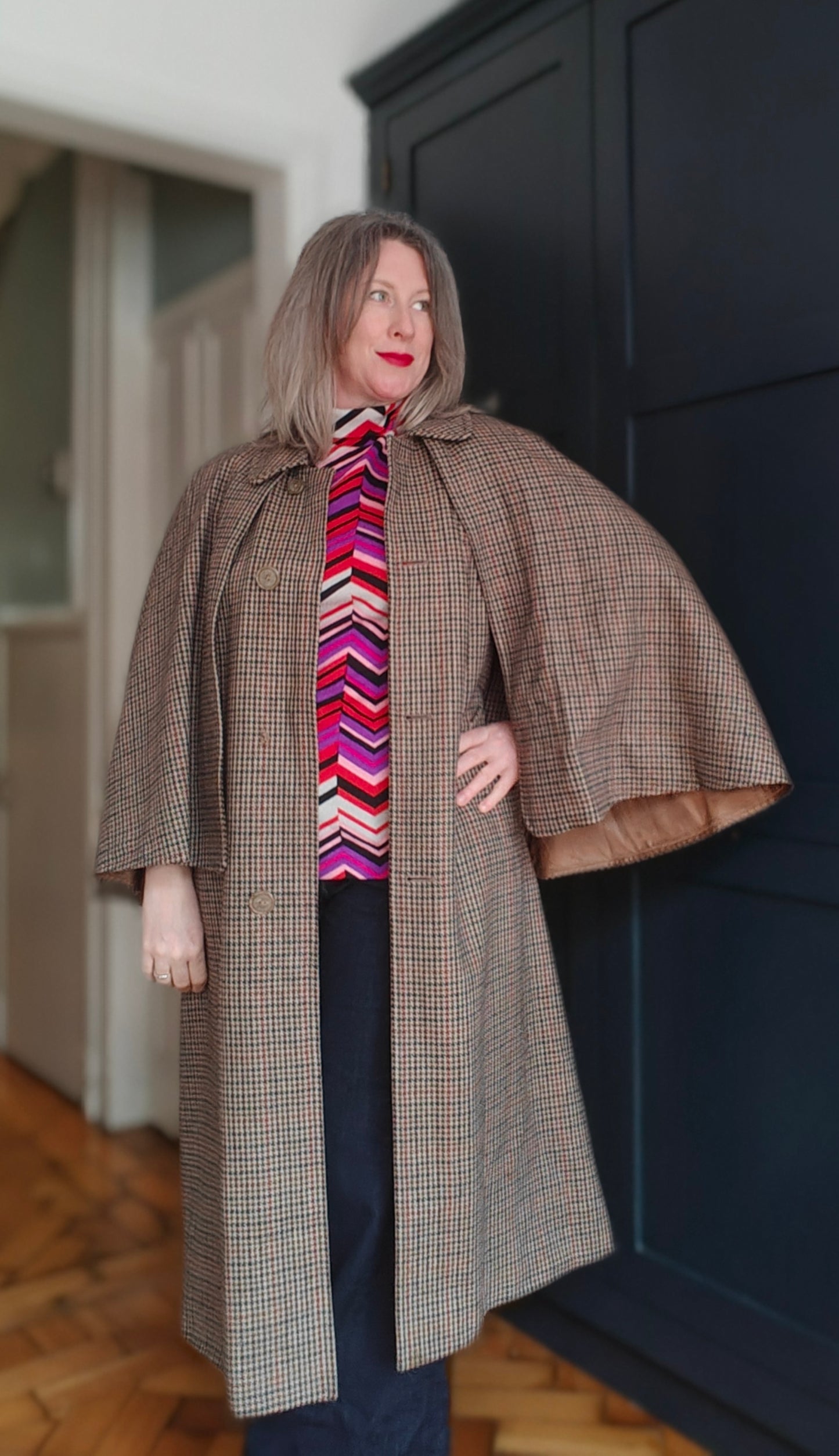 Woman wearing a long brown coat over a colorful striped shirt indoors.