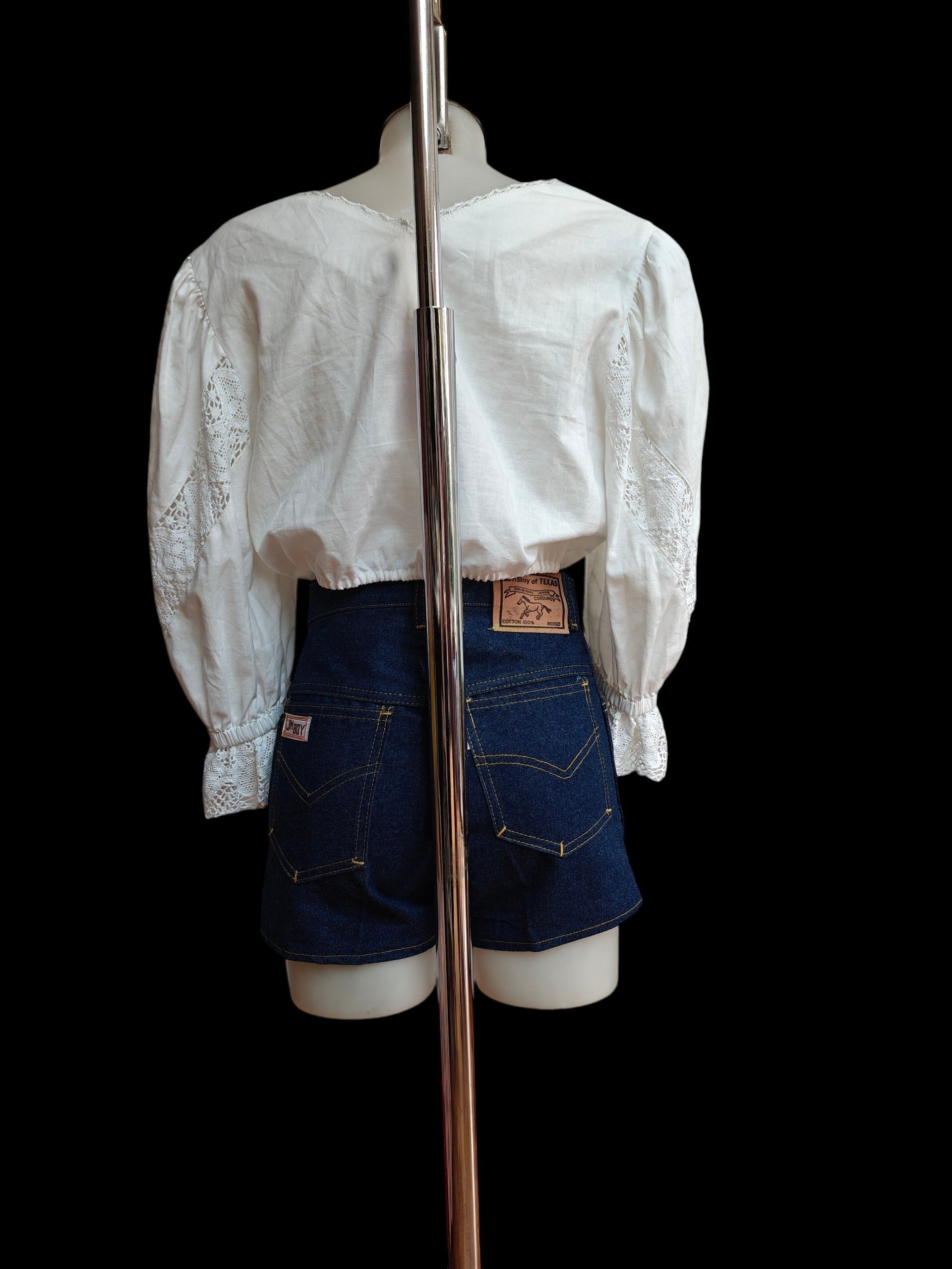 Mannequin wearing a white blouse and blue denim shorts on a black background