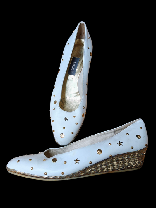 White wedge shoes with gold studs on a black background