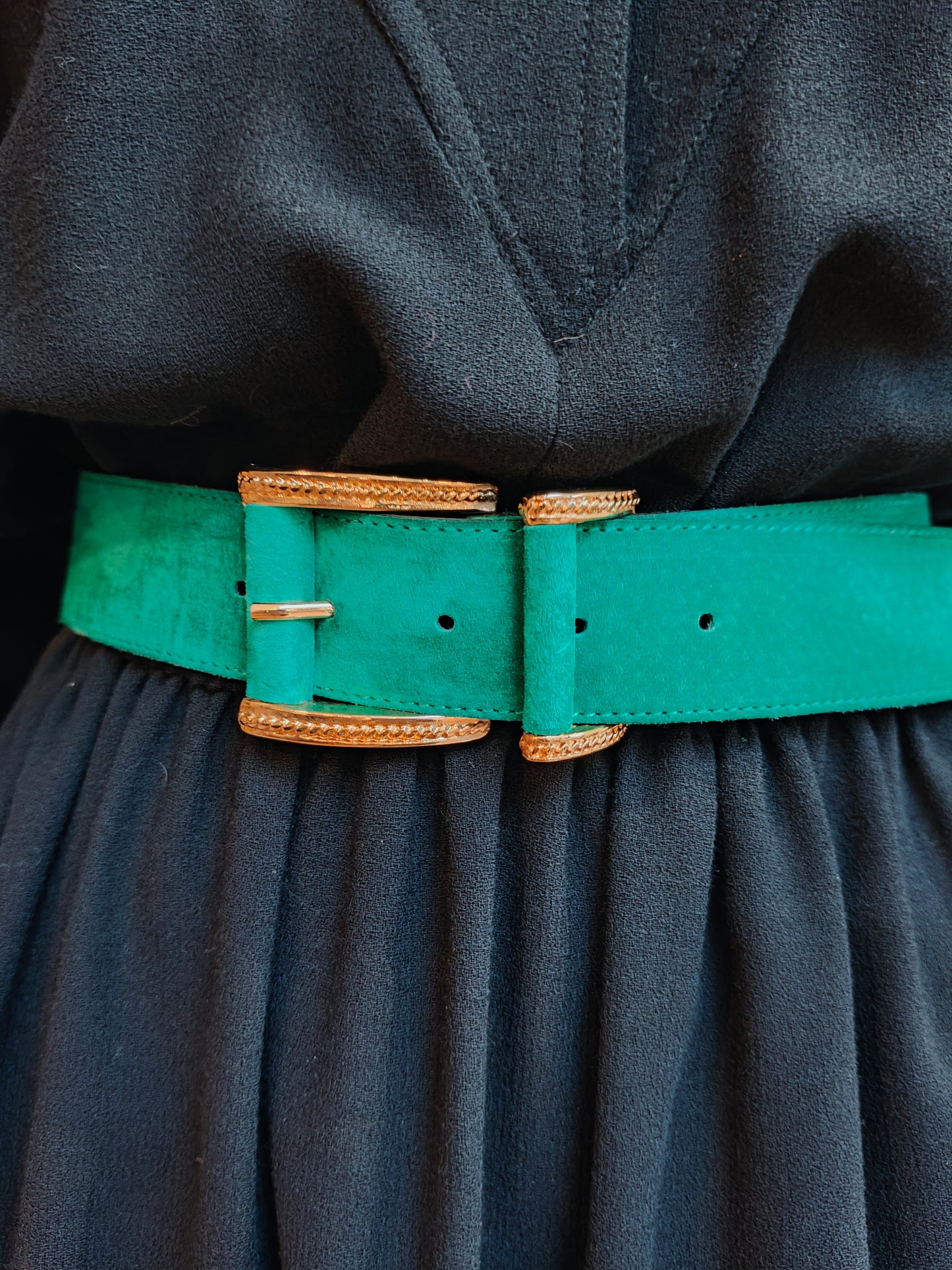 Green belt with gold buckle on a dark fabric background