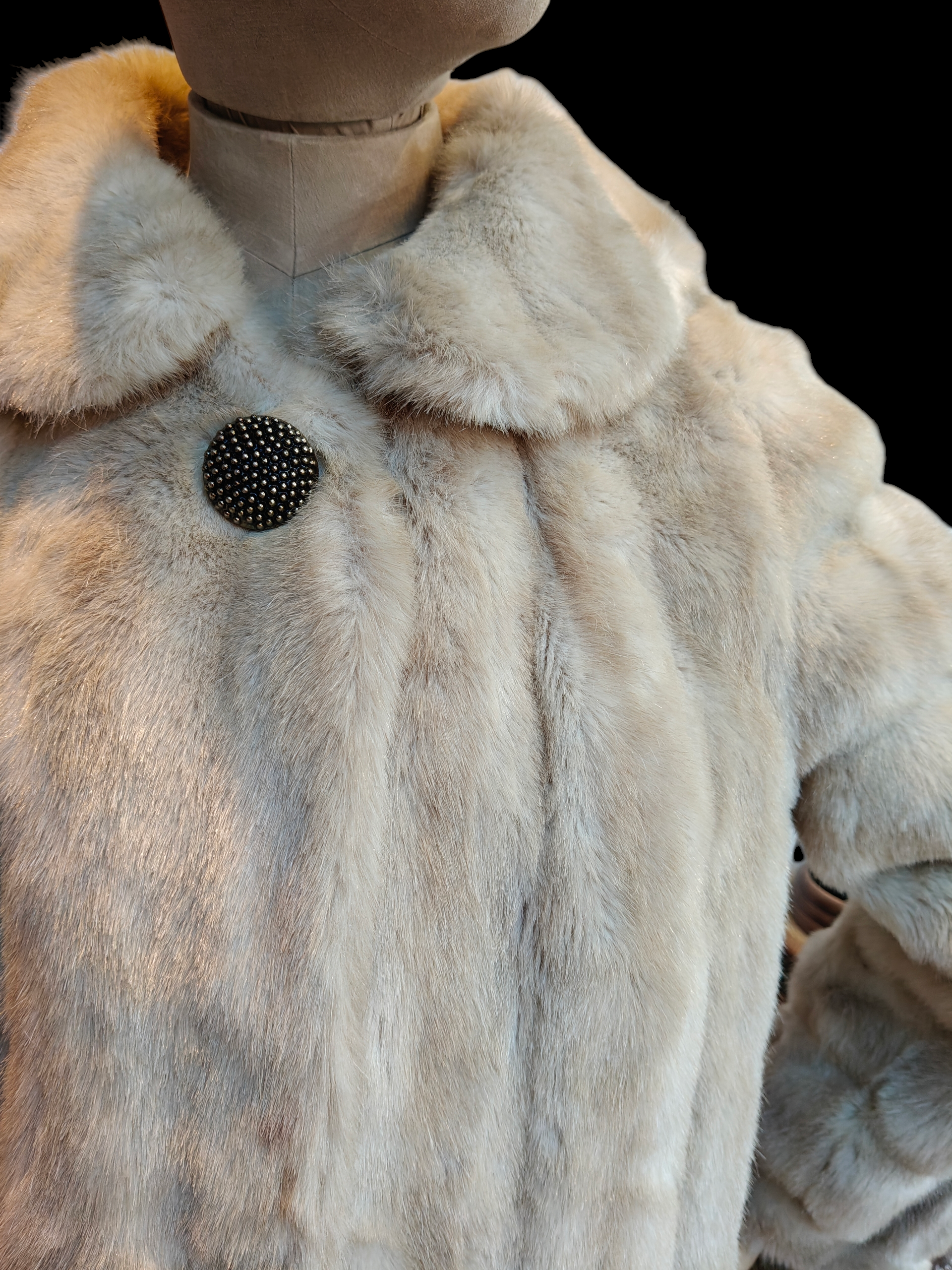 Close-up of a fur coat with a black button on a mannequin against a black background