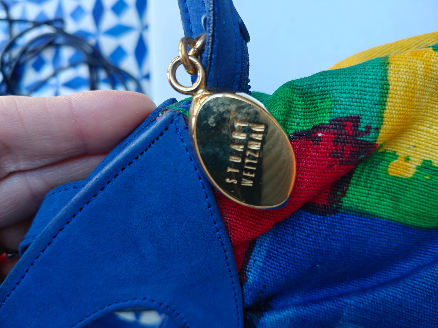 Stuart Weitzman gold tag on a colorful fabric background