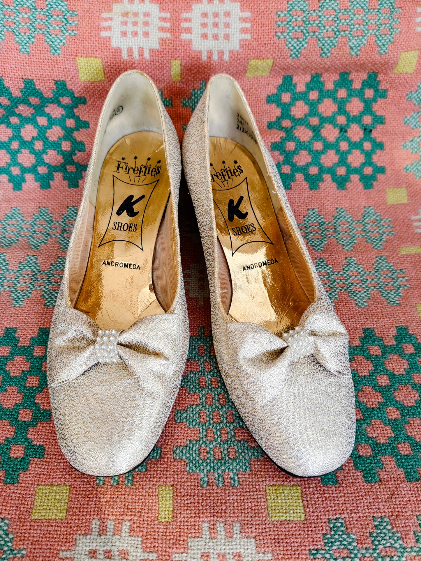 Pair of glittery shoes with a bow on a patterned fabric background