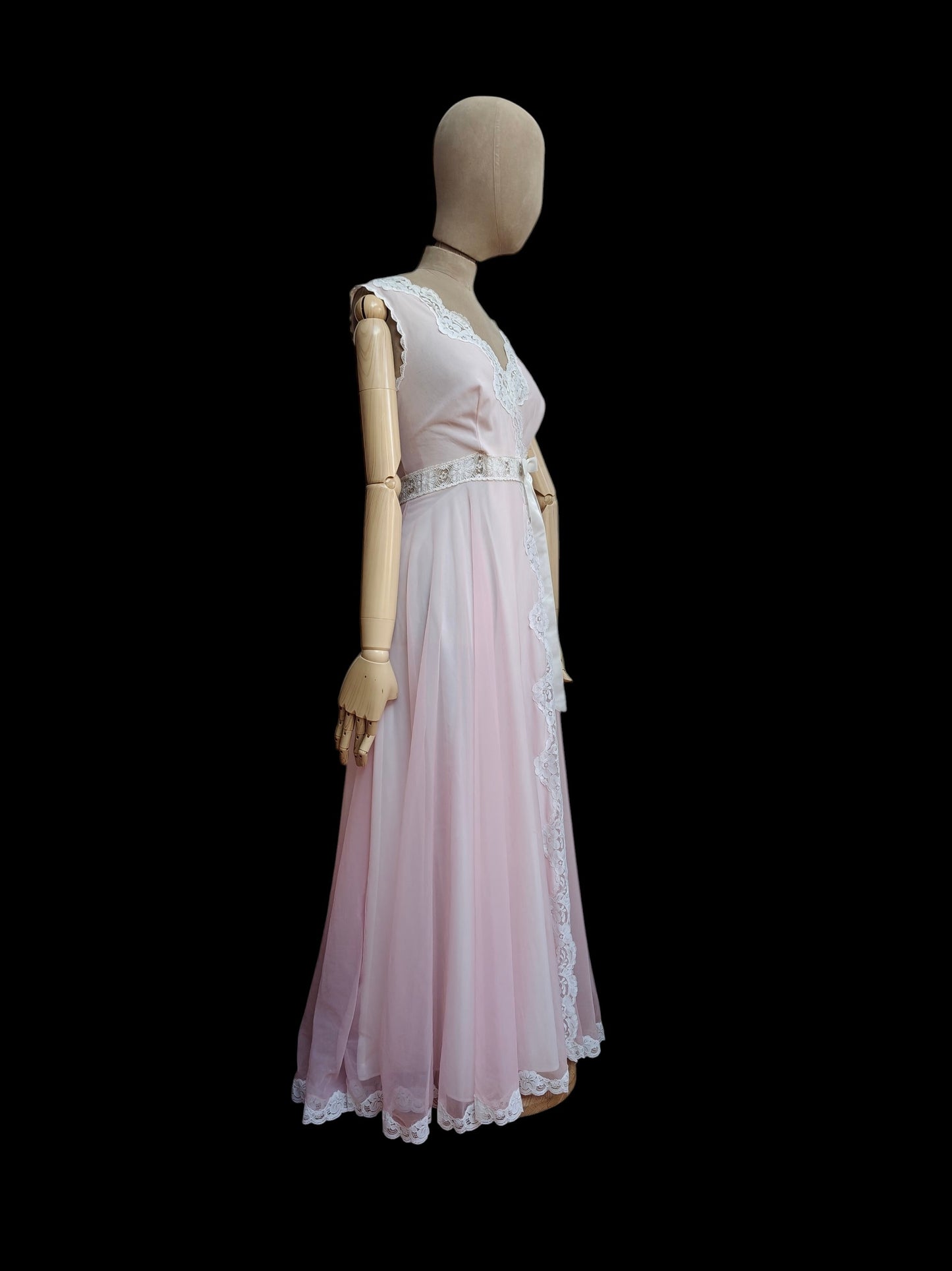 A light pink and white sleeveless maxi dress displayed on a wooden mannequin against a solid black background.