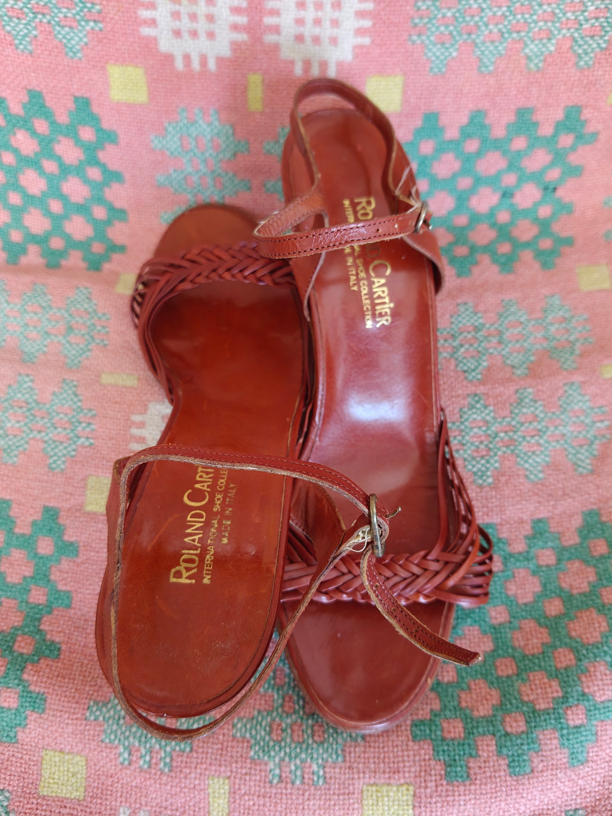 Brown sandal with 'Roland Cartier' branding on a patterned pink and green background