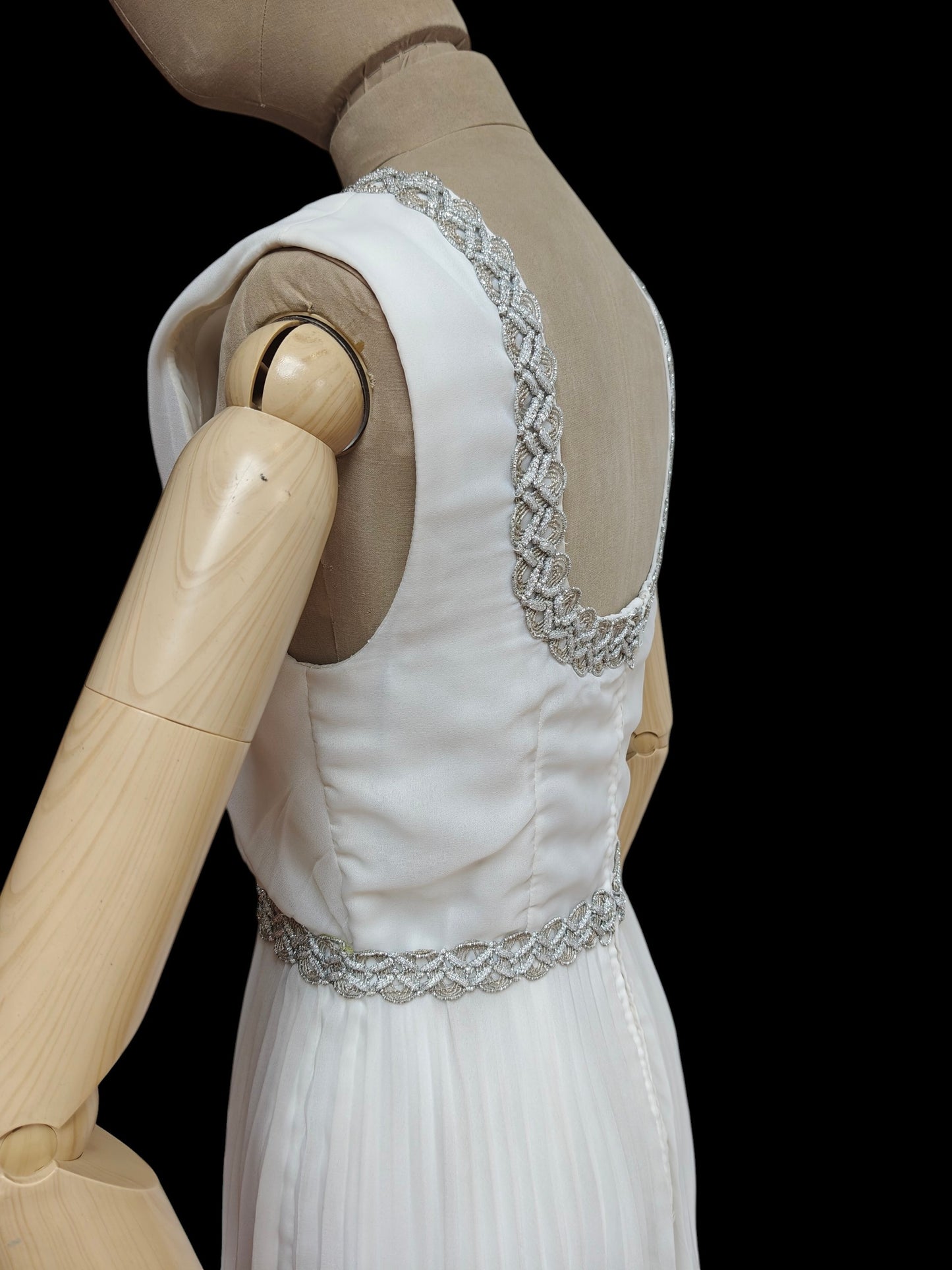 White wedding dress with silver embellishments on a mannequin against a black background