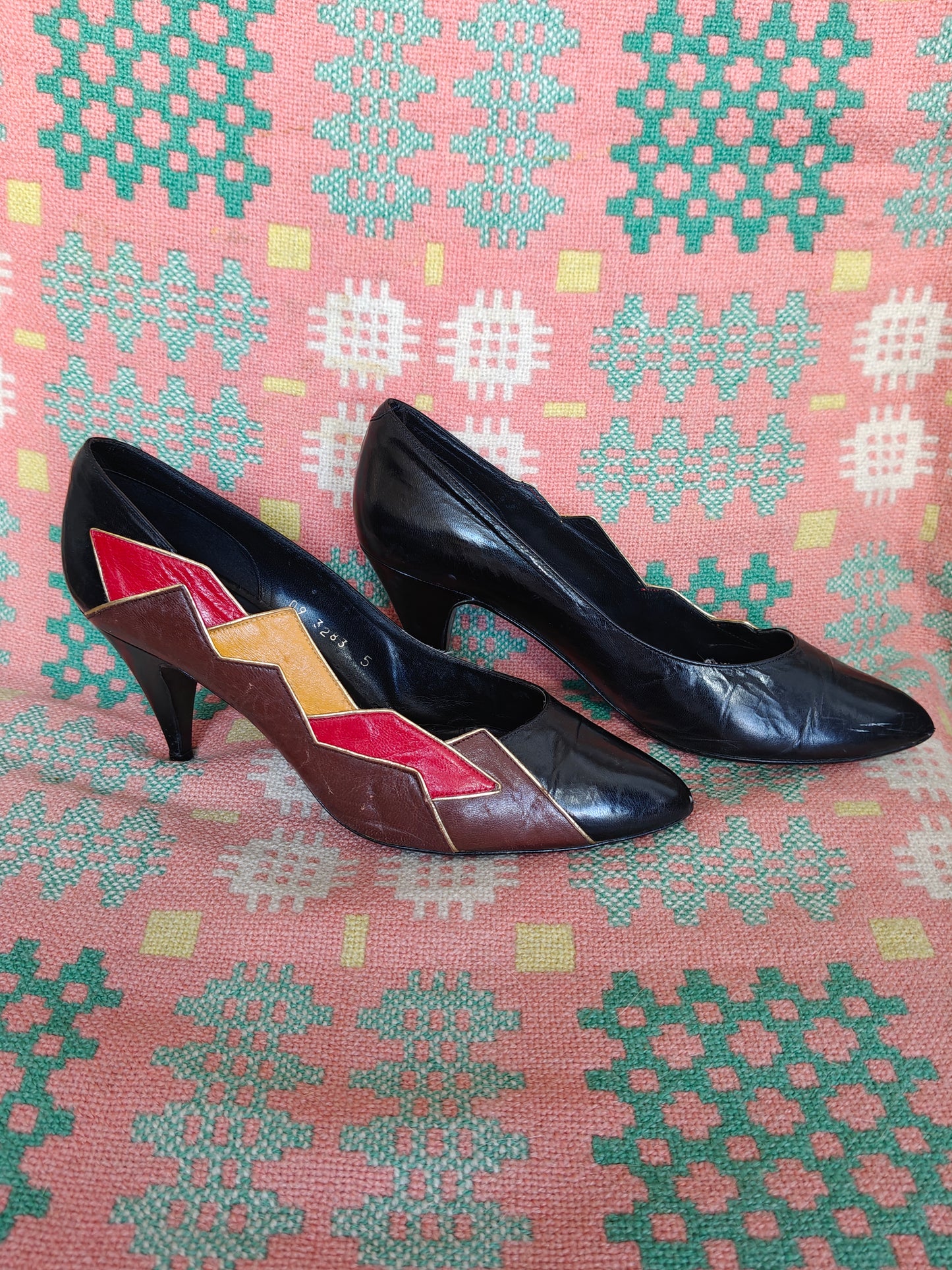 Pair of black high-heeled shoes with geometric pattern on a pink fabric background