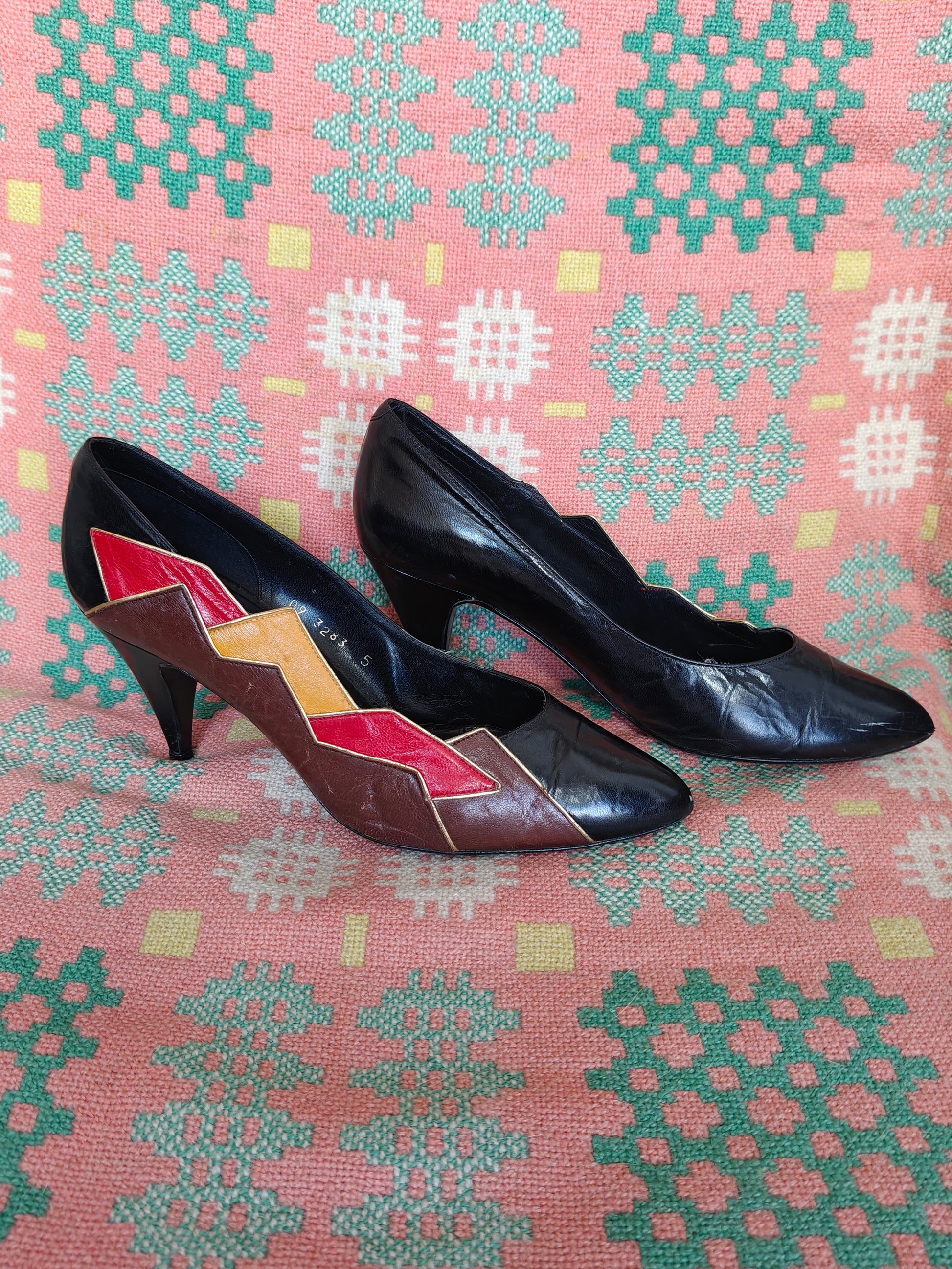 Pair of black high-heeled shoes with geometric pattern on a pink fabric background