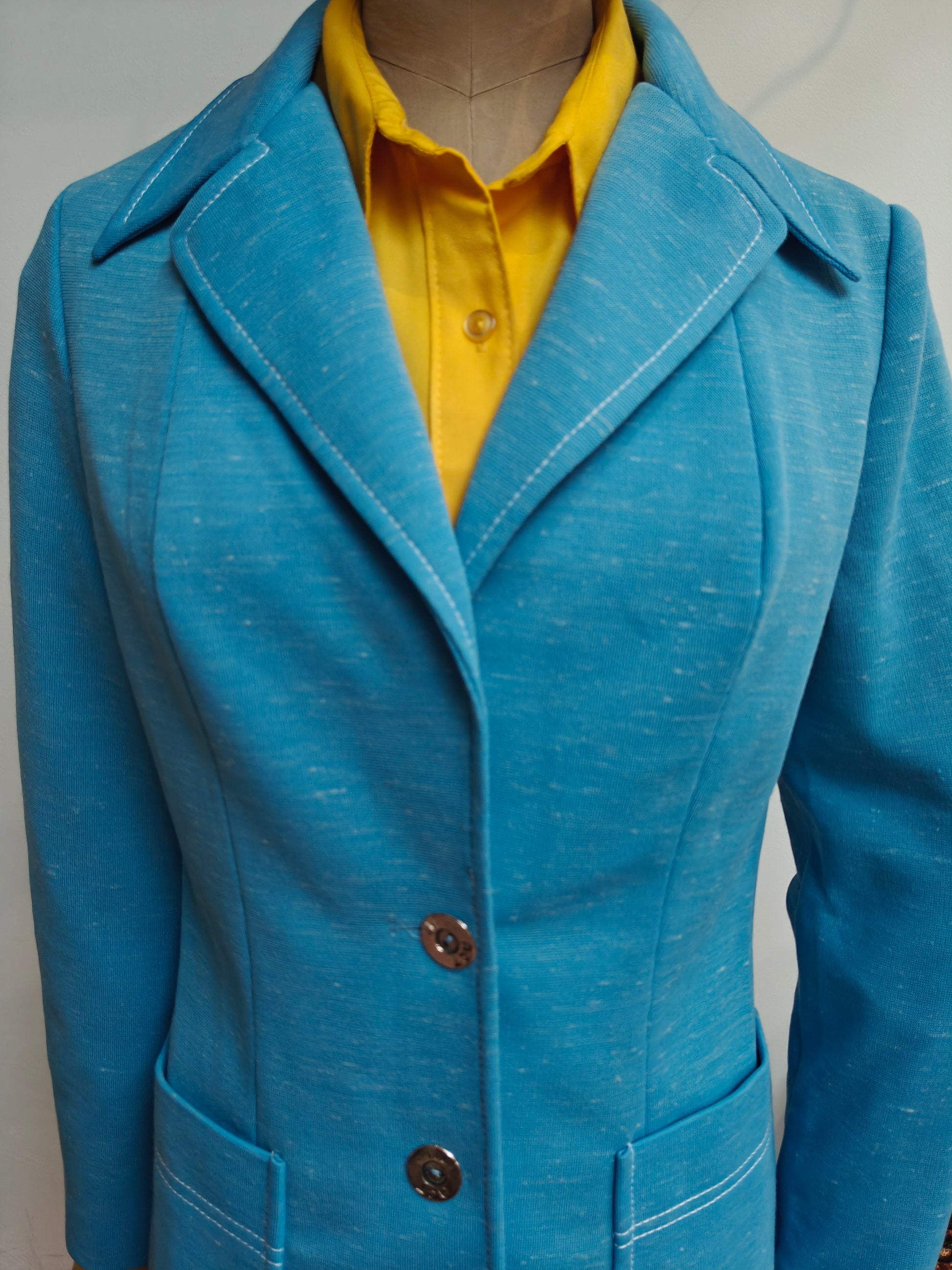 A bright blue textured blazer with white contrast stitching, worn over a yellow collared shirt on a mannequin.