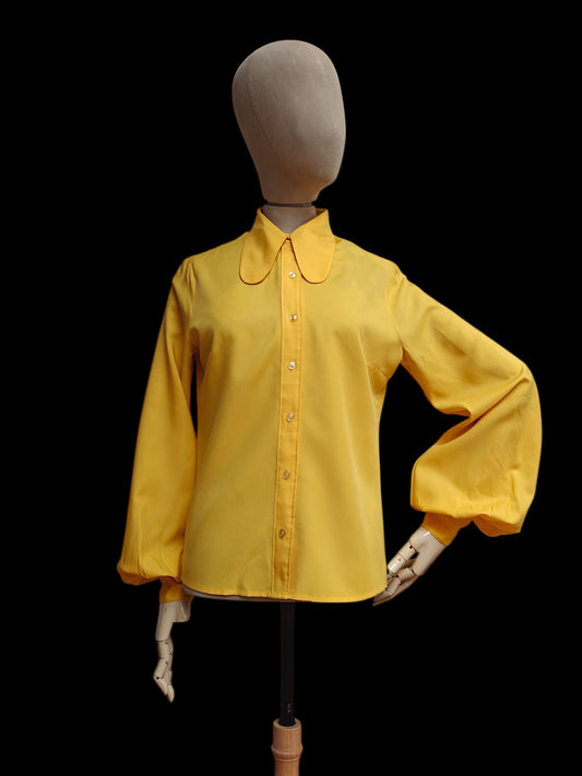A bright yellow long-sleeve 1960s blouse with a beagle collar and button front, displayed on a mannequin against a solid black background.