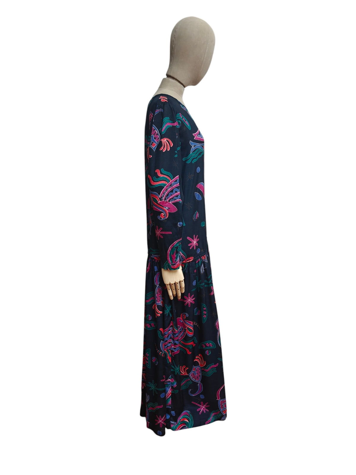 A long-sleeve maxi dress with a vibrant multicolor abstract pattern on a dark navy base, displayed on a mannequin against a plain white background.