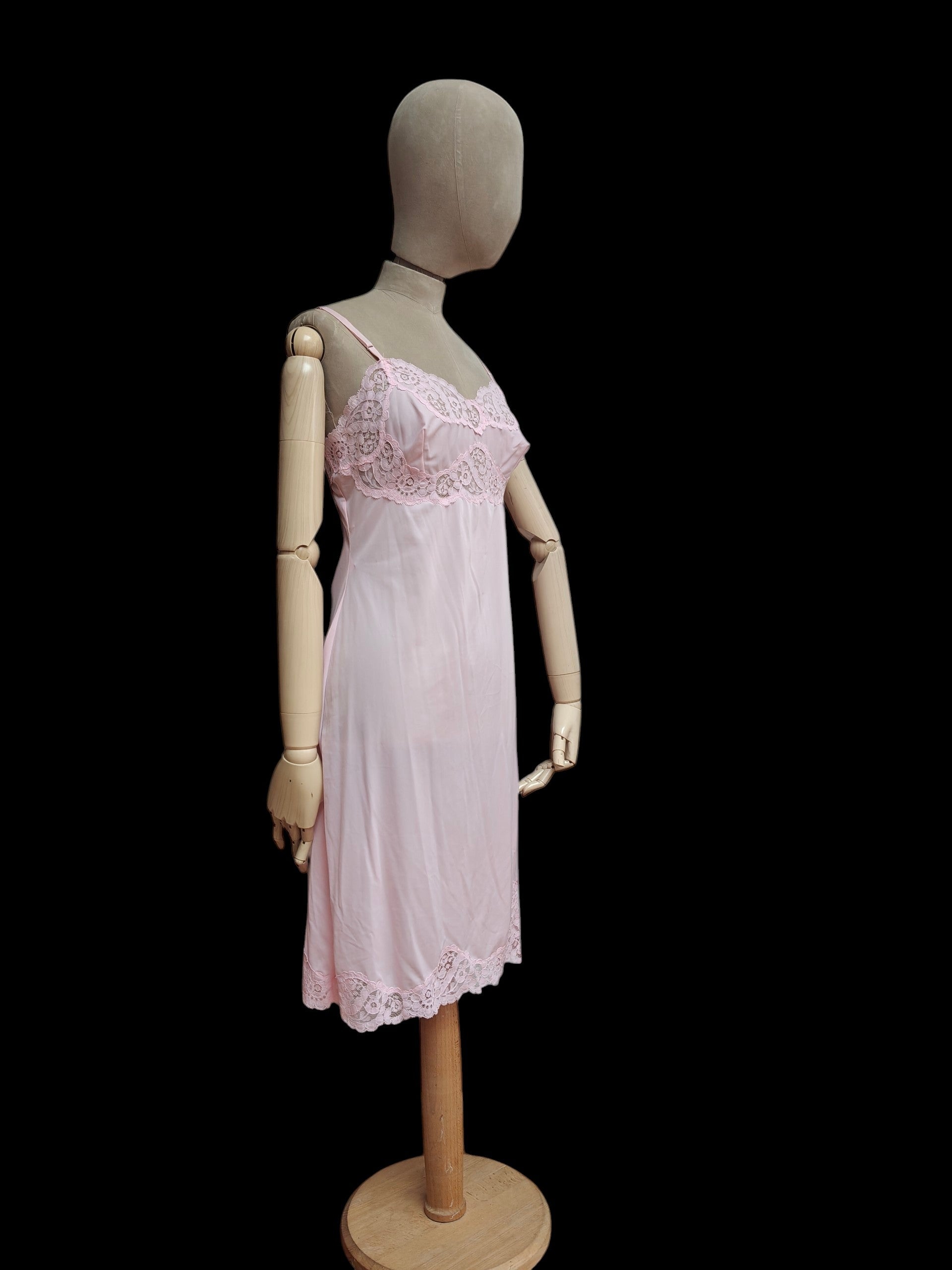 A light pink sheer babydoll nightgown with floral lace trim on the bodice and hem, displayed on a wooden mannequin against a solid black background.