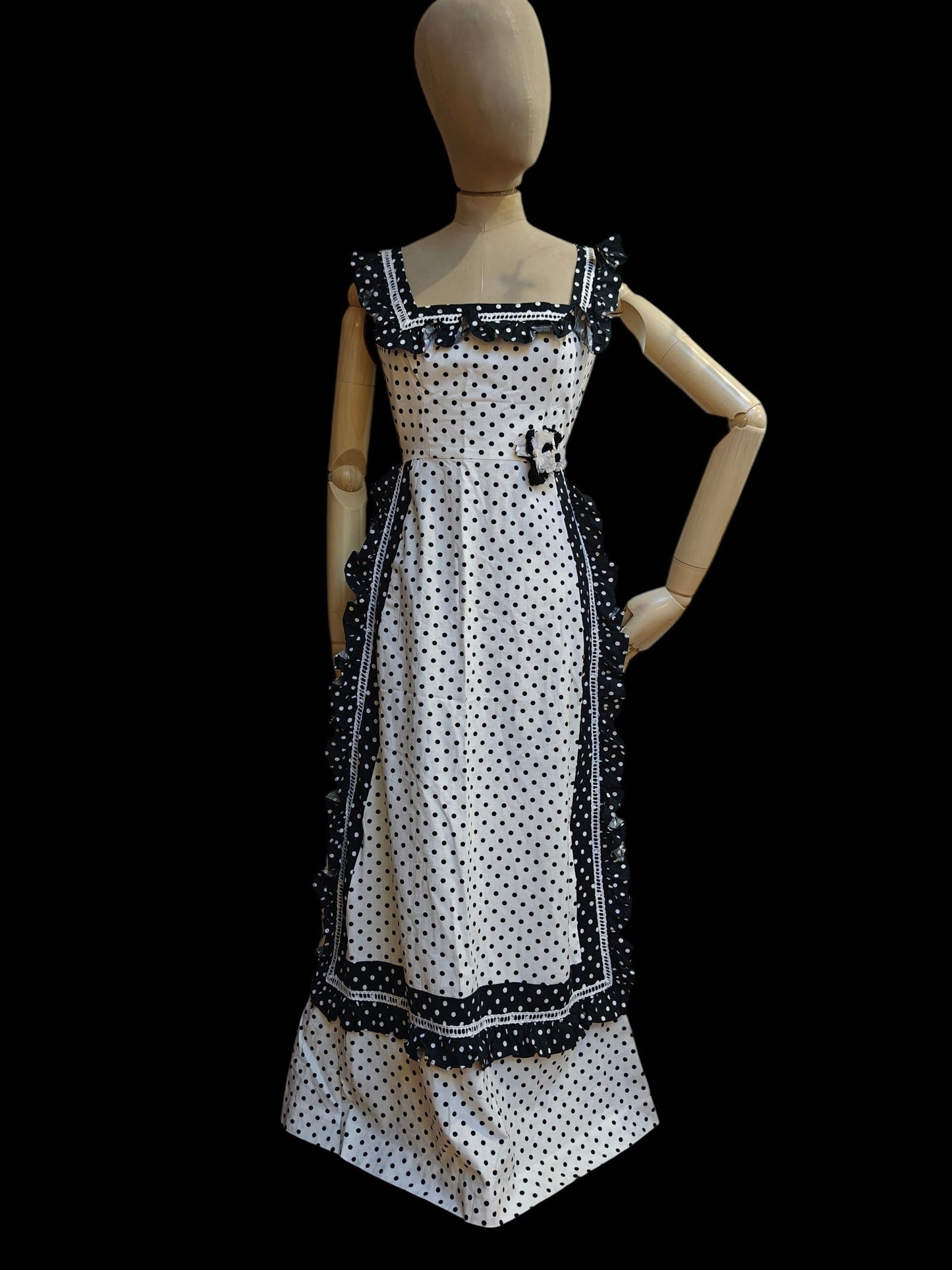 Mannequin wearing a black and white polka dot dress with decorative trim on a black background