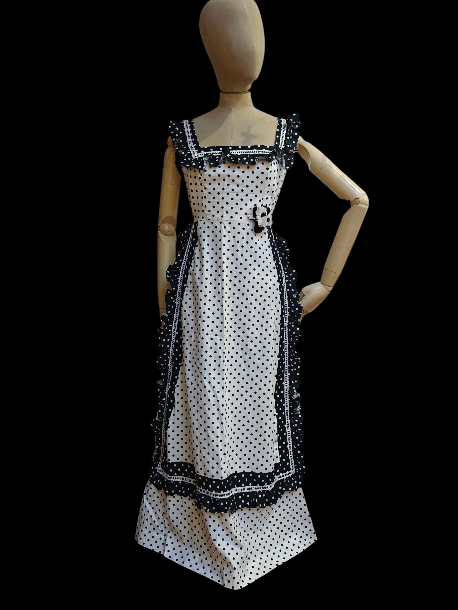 Mannequin wearing a black and white polka dot dress with decorative trim on a black background