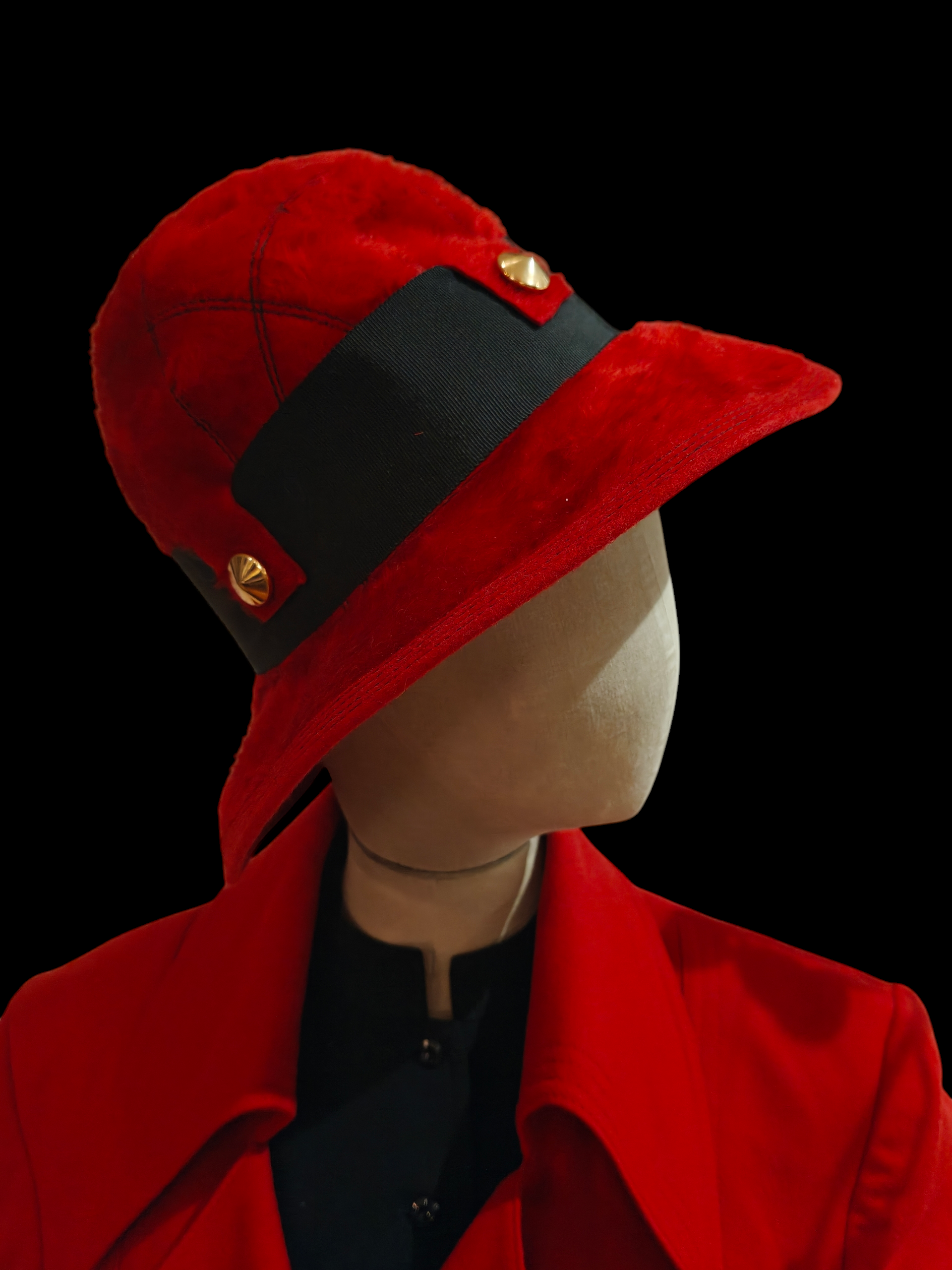 Red hat with black band and gold buttons on a mannequin against a black background