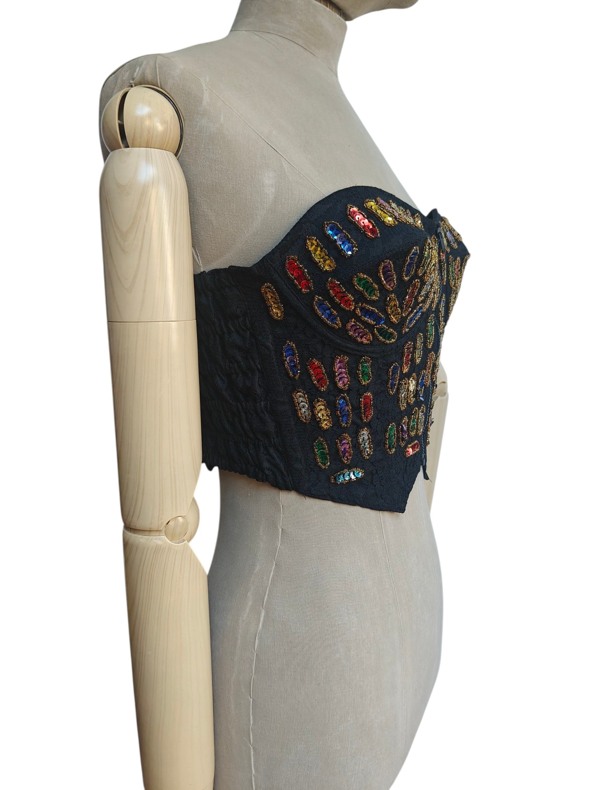 A black strapless bustier-style top with colorful sequined embellishments, displayed on a beige fabric mannequin torso against a white background.