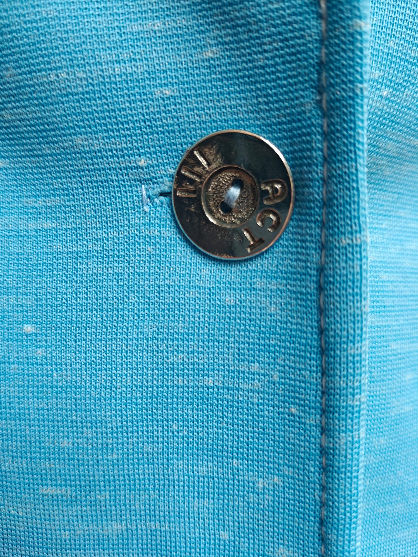 Close-up of a textured turquoise blue fabric garment with a silver metal button.