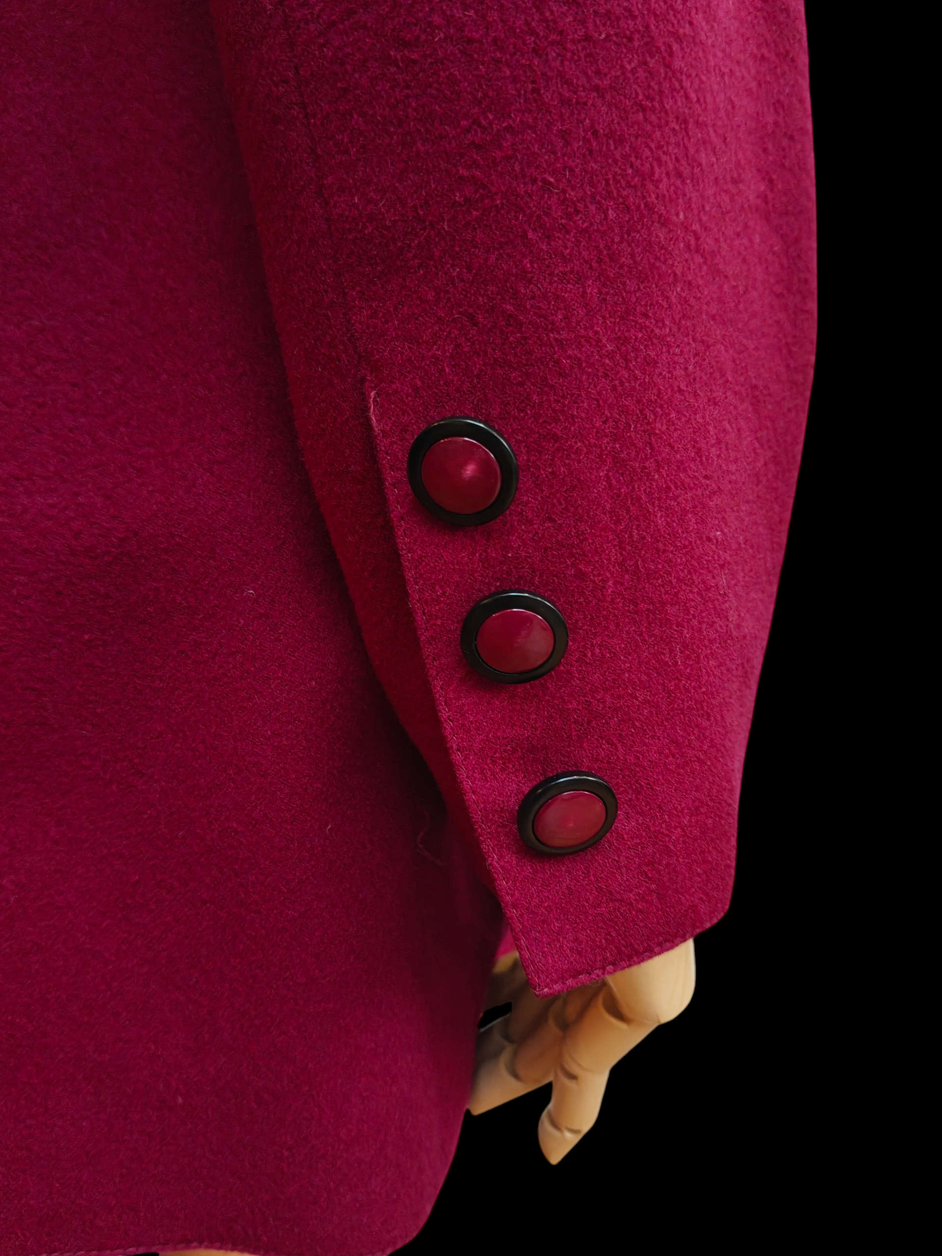 Close-up of a magenta coat with three buttons on a black background