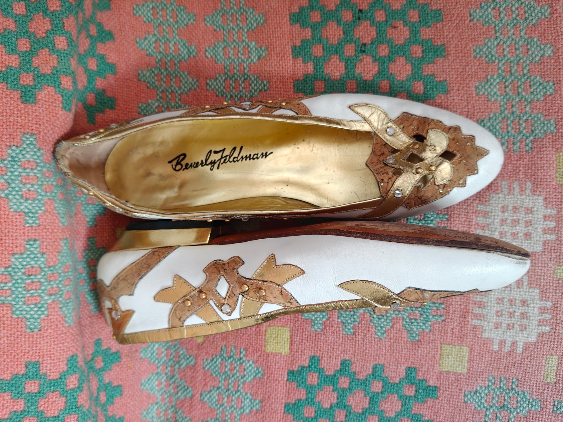 Pair of white shoes with gold embellishments on a patterned fabric background