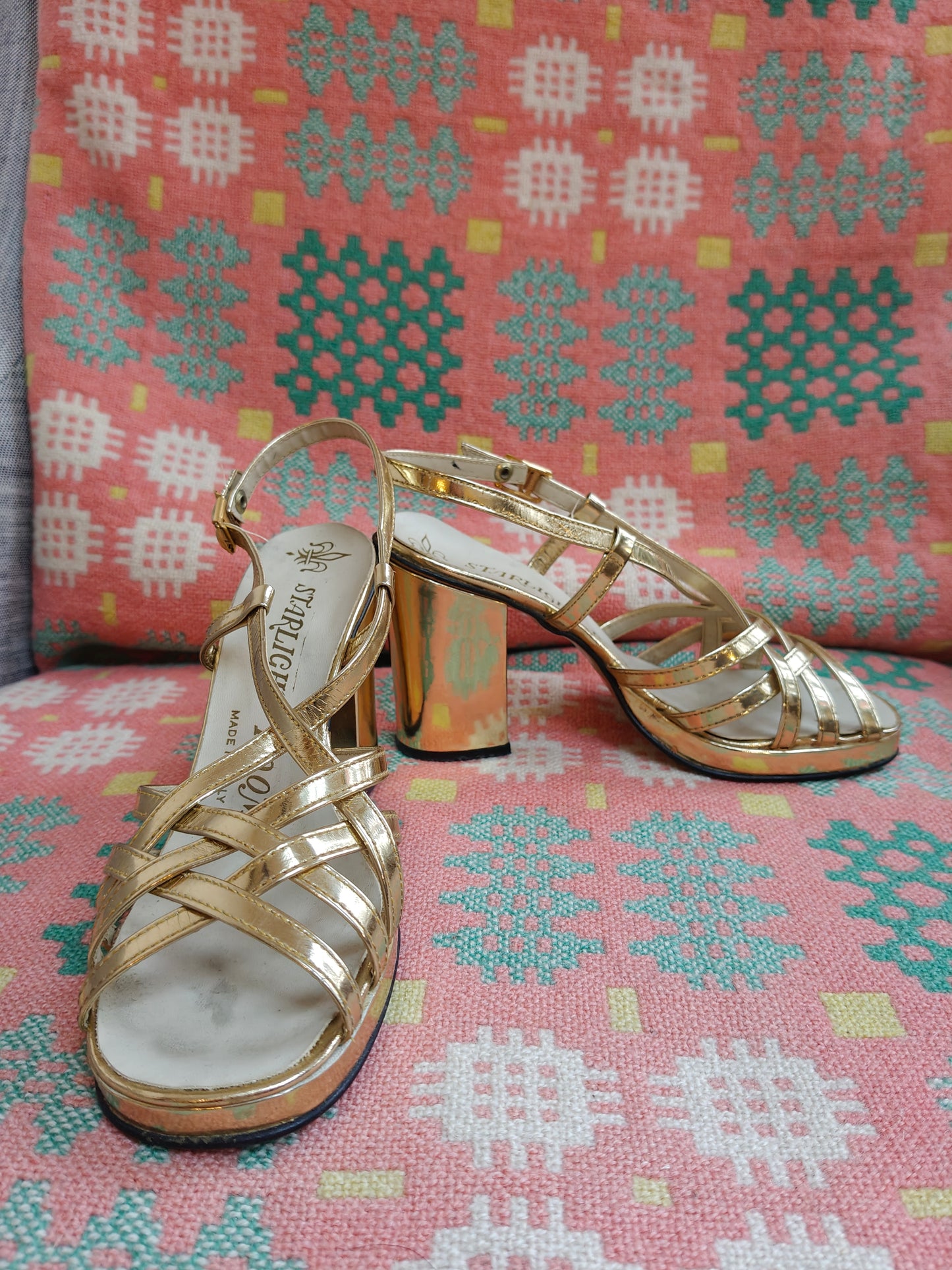 Gold high-heeled sandals on a patterned fabric background