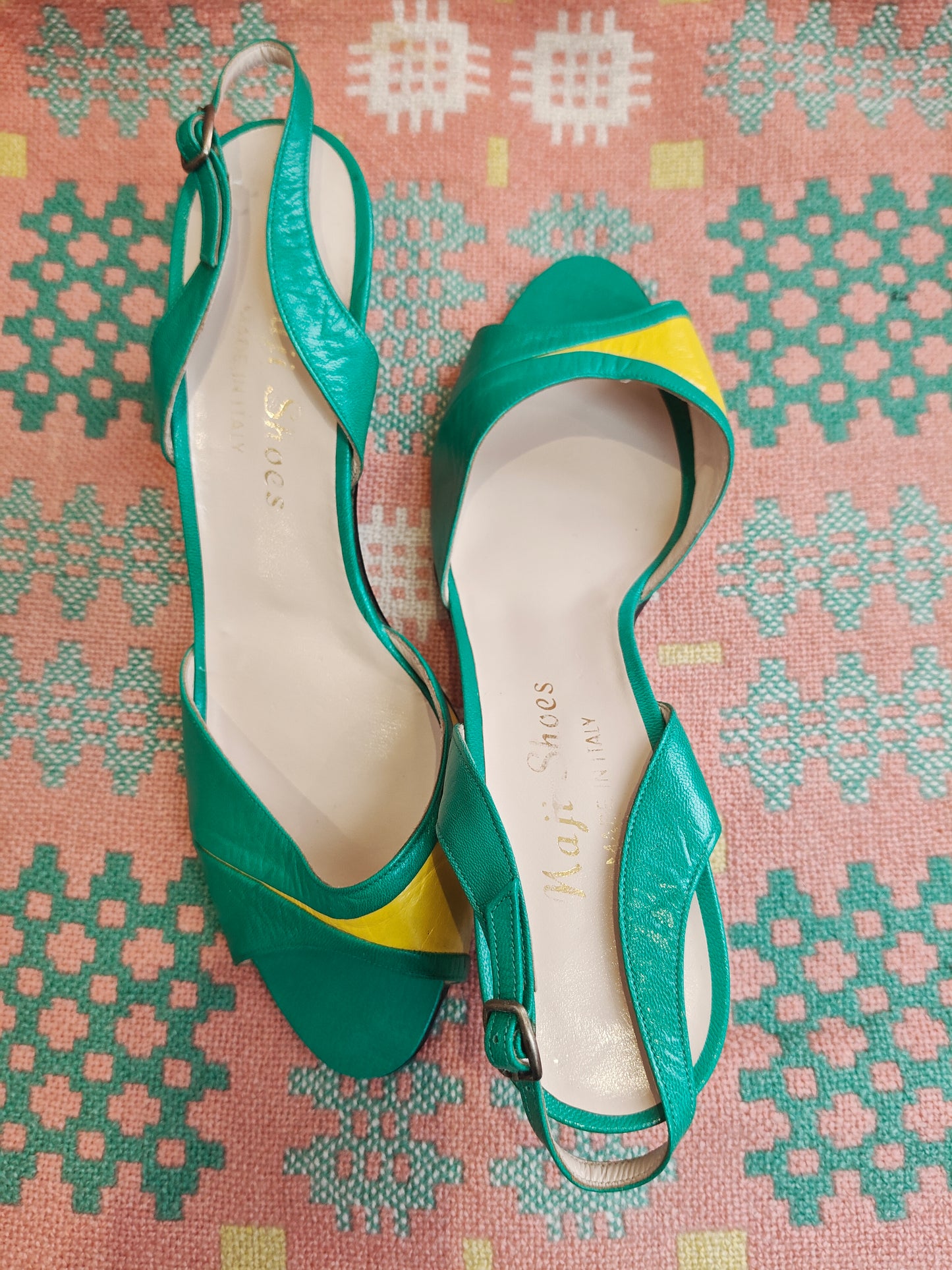 Green high-heeled shoes with yellow accents on a patterned fabric background