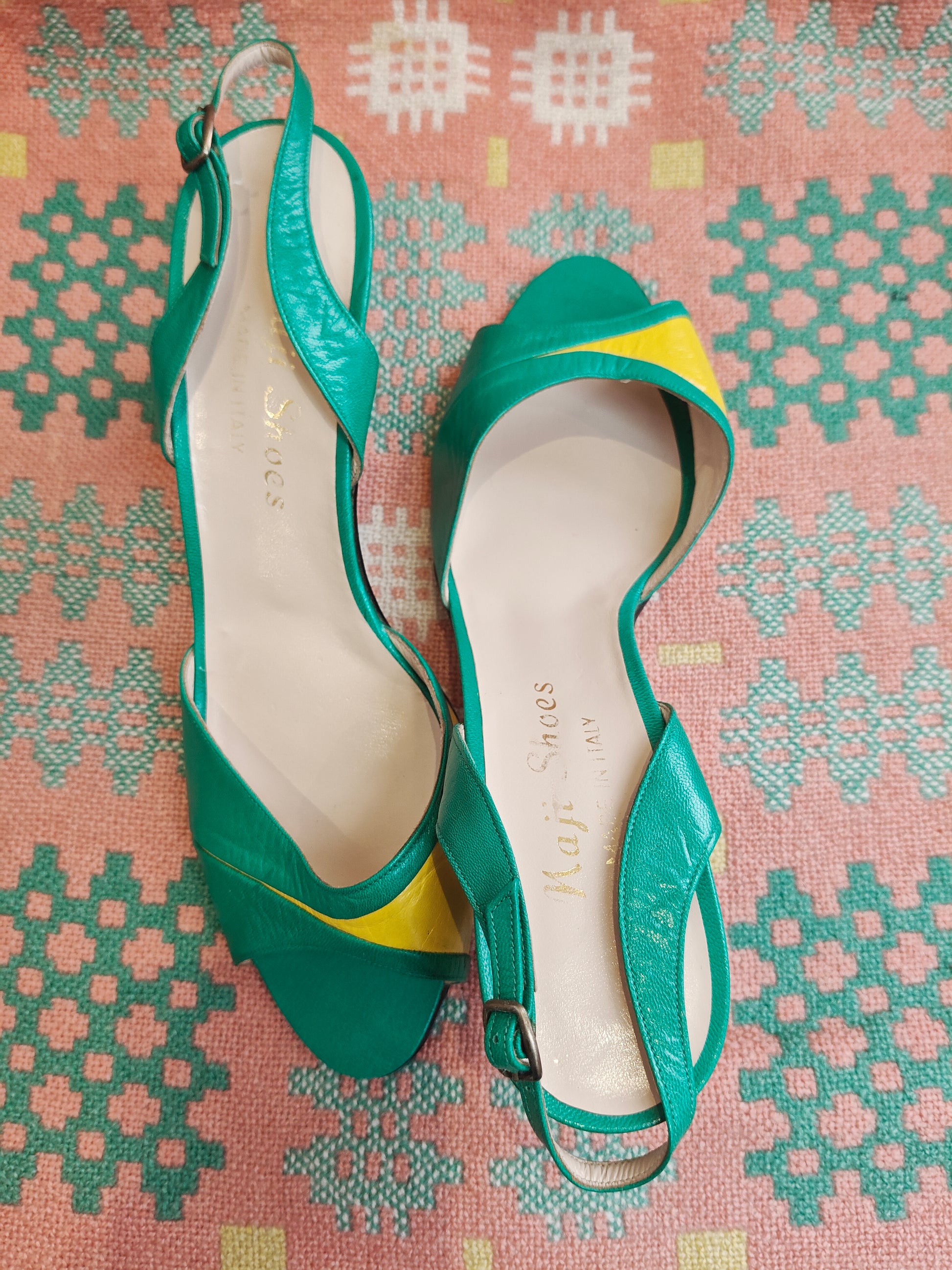 Green high-heeled shoes with yellow accents on a patterned fabric background