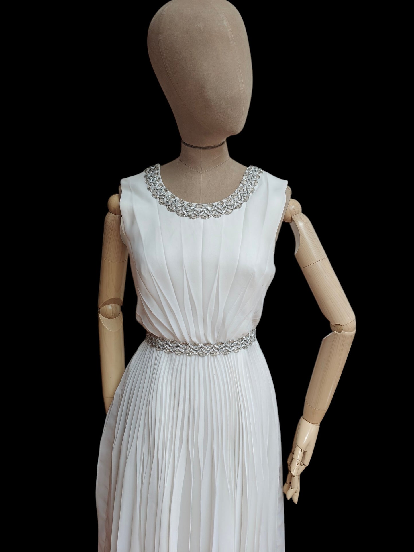 Mannequin wearing a white dress with decorative waistband on a black background