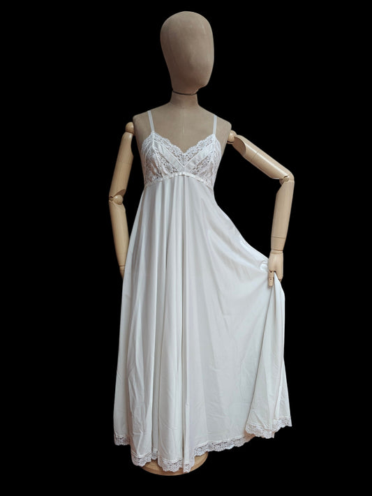 A white nightgown or slip dress with lace trim and spaghetti straps, displayed on a wooden mannequin against a solid black background.